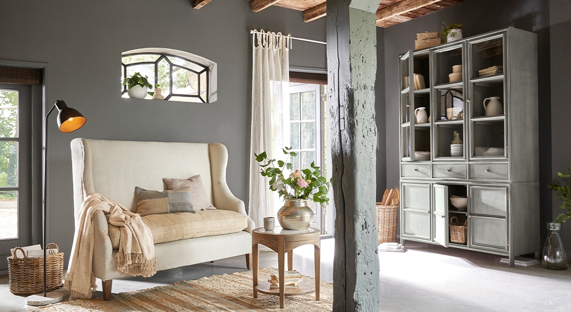 Gezellige woonkamer met grijze houten vitrinekast en crème bank op houten poten, natuurlijke decoratie