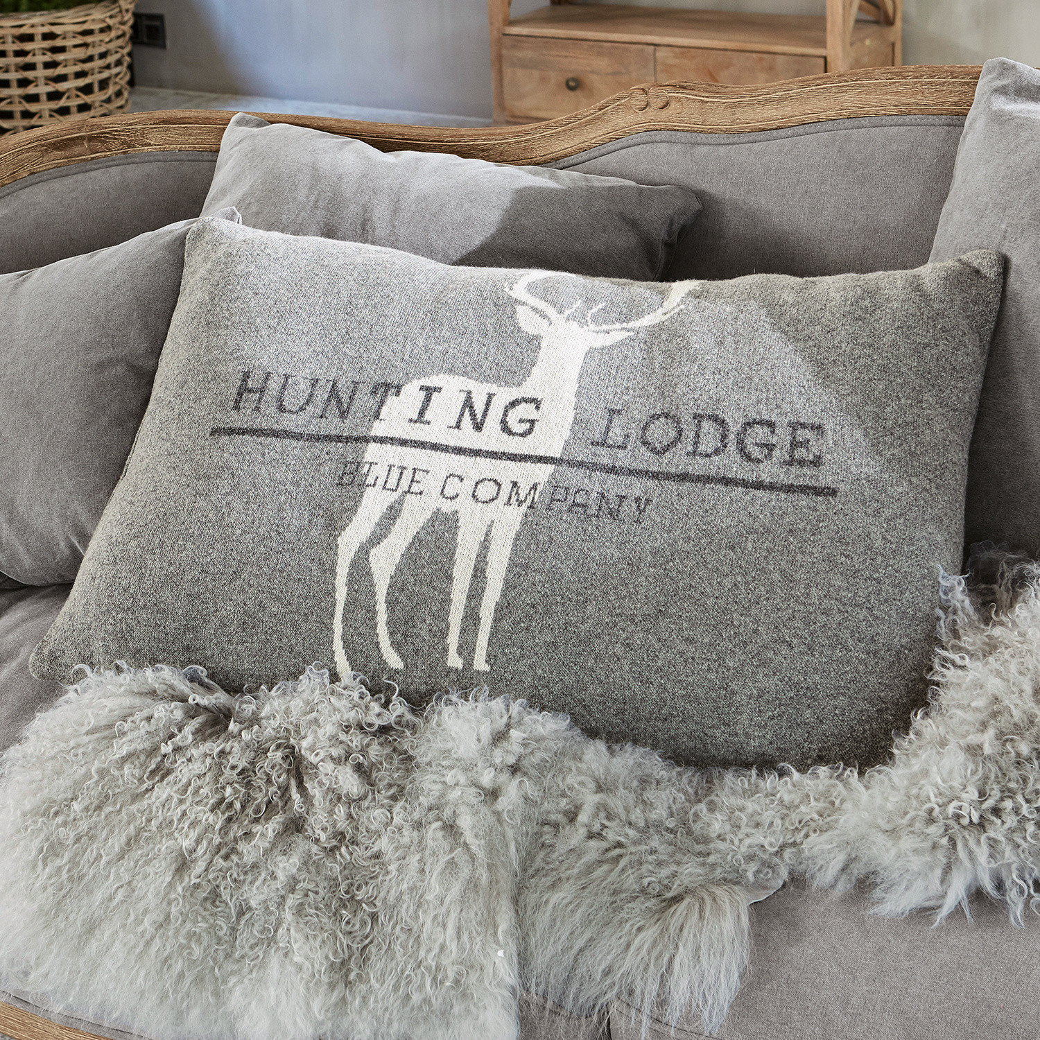 Kussen Lodge Grijs sierkussen met hertmotief en tekst op zachte bank met bontdeken