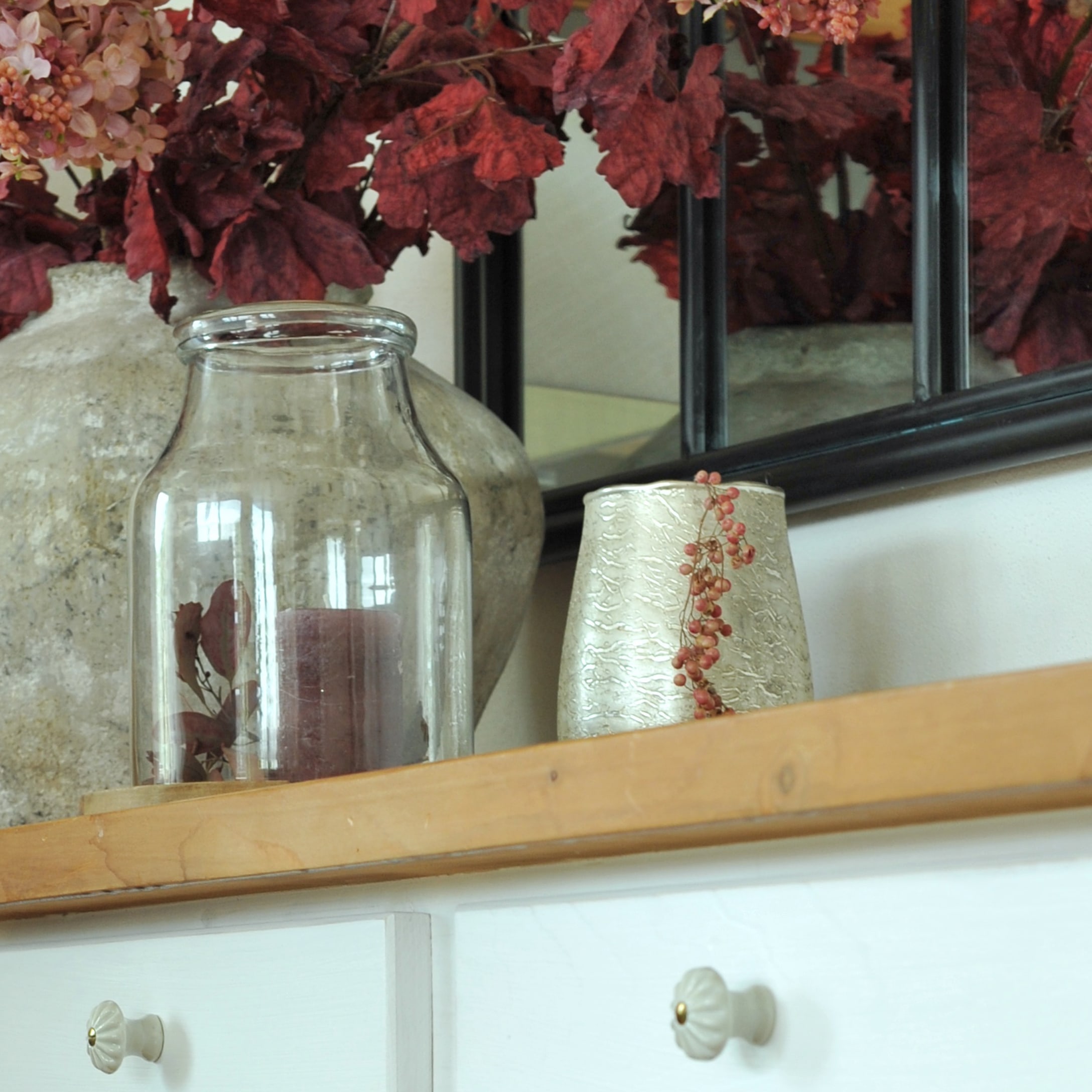 Transparante glazen vaas met bordeauxrode kaars op houten plank met rode bladdecoratie