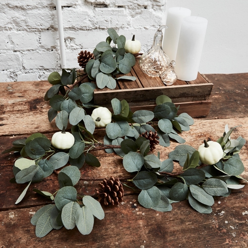 Decoratieve krans van groene eucalyptusbladeren, witte mini-pompoenen en dennenappels op houten tafel