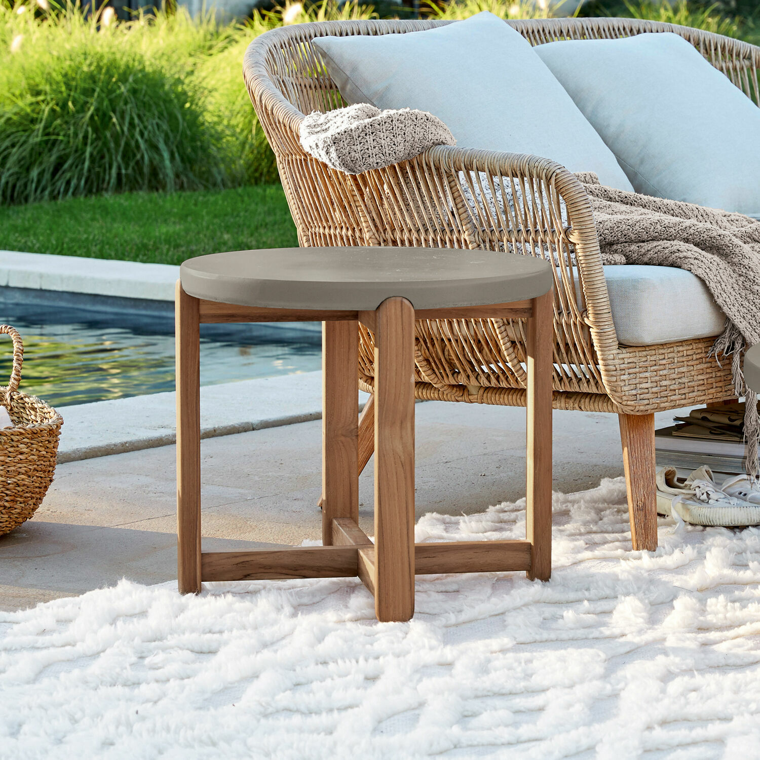 Ronde tafel met houten onderstel en grijs blad op terras bij zwembad met vloerkleed en rotan stoel