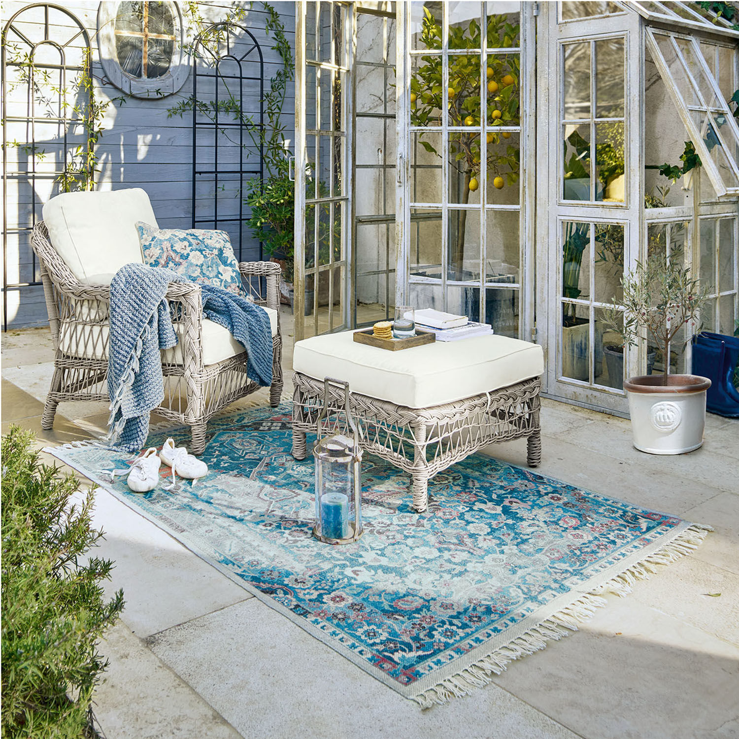 Tuinmeubelset van grijs rattan met crèmekleurige kussens en blauwe vloerkleed voor terras