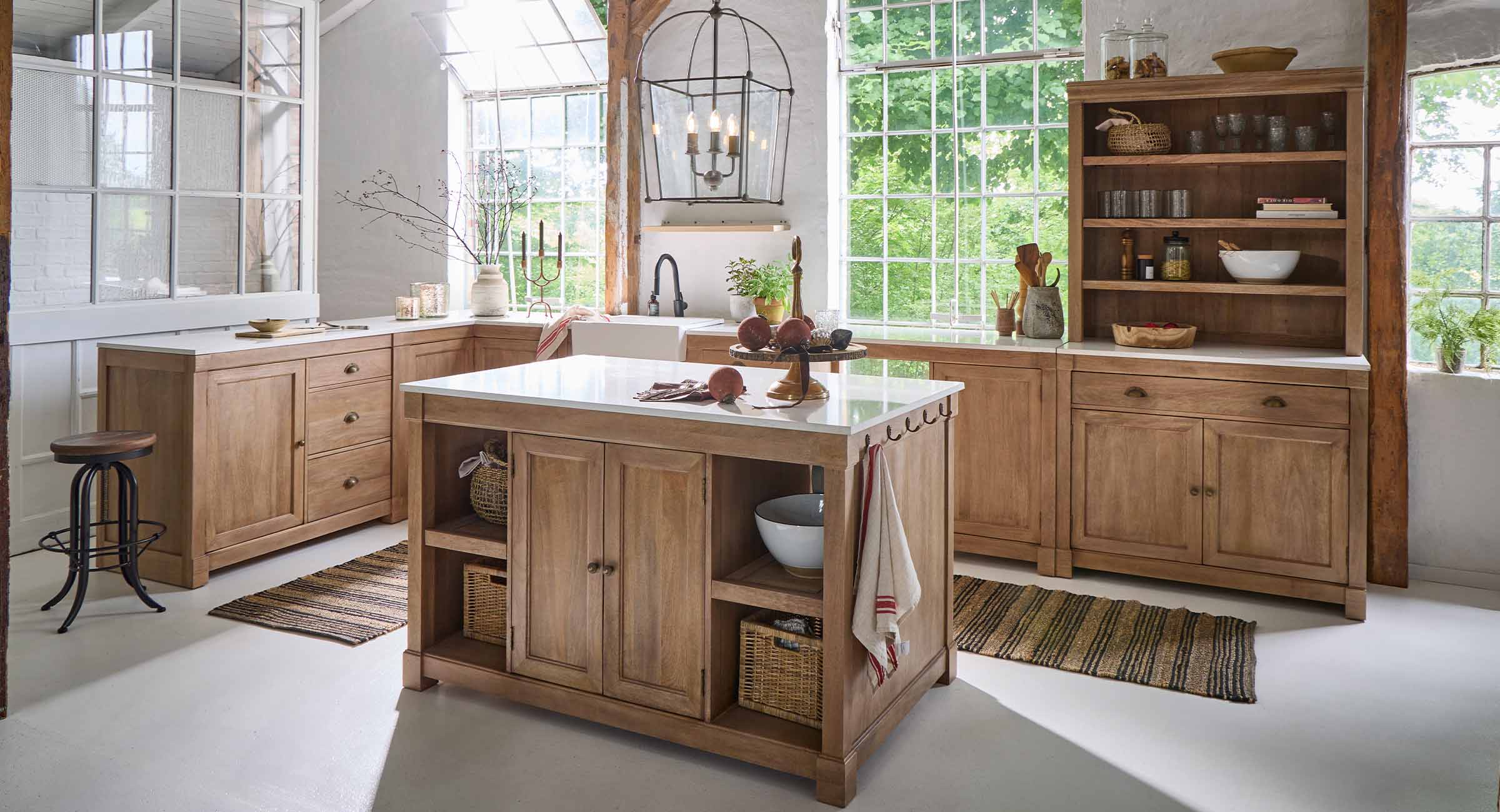Keuken met eiland en eikenhouten kasten in natuurlijke kleur, witte werkbladen en grote ramen