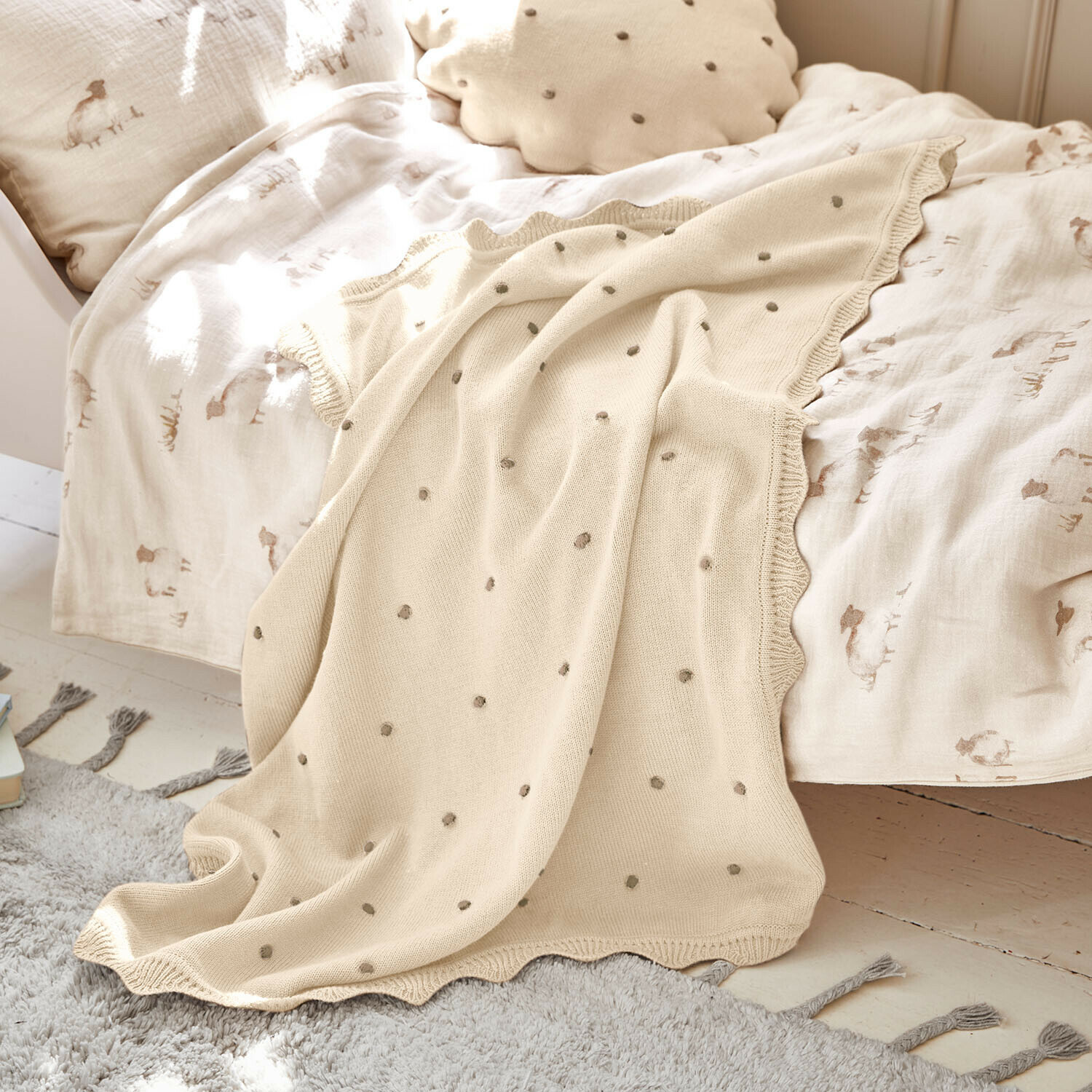 Plaid Saphie Beige gebreide deken met grijze stippen op bed met licht beddengoed en natuurlijke kussen