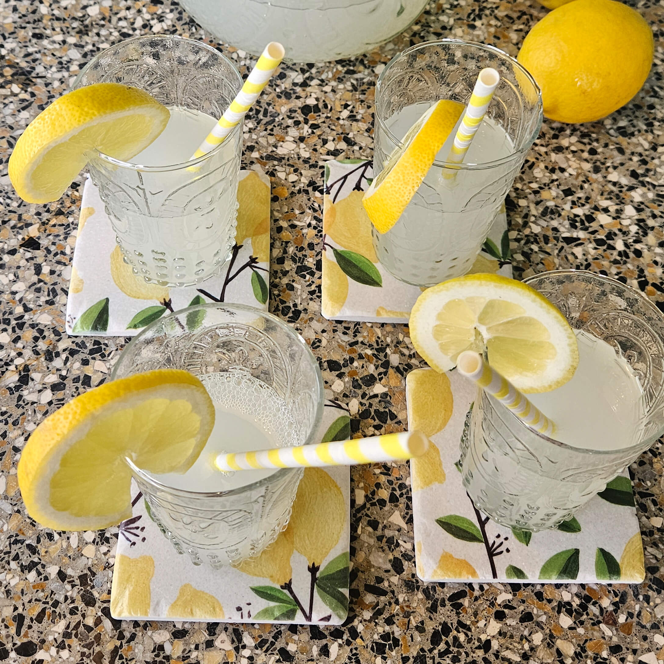 Glazen limonade met citroenschijfjes op keramische onderzetters met citroendesign op stenen aanrecht