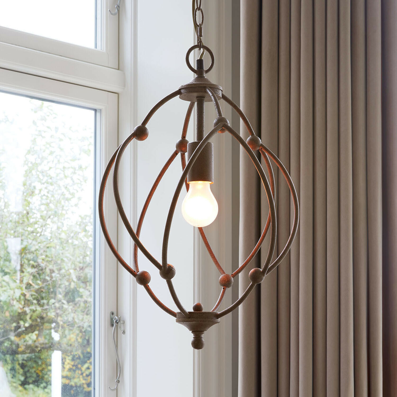 Hanglamp van roestig metaal met bolvormig frame en zichtbare gloeilamp voor rustieke sfeer.