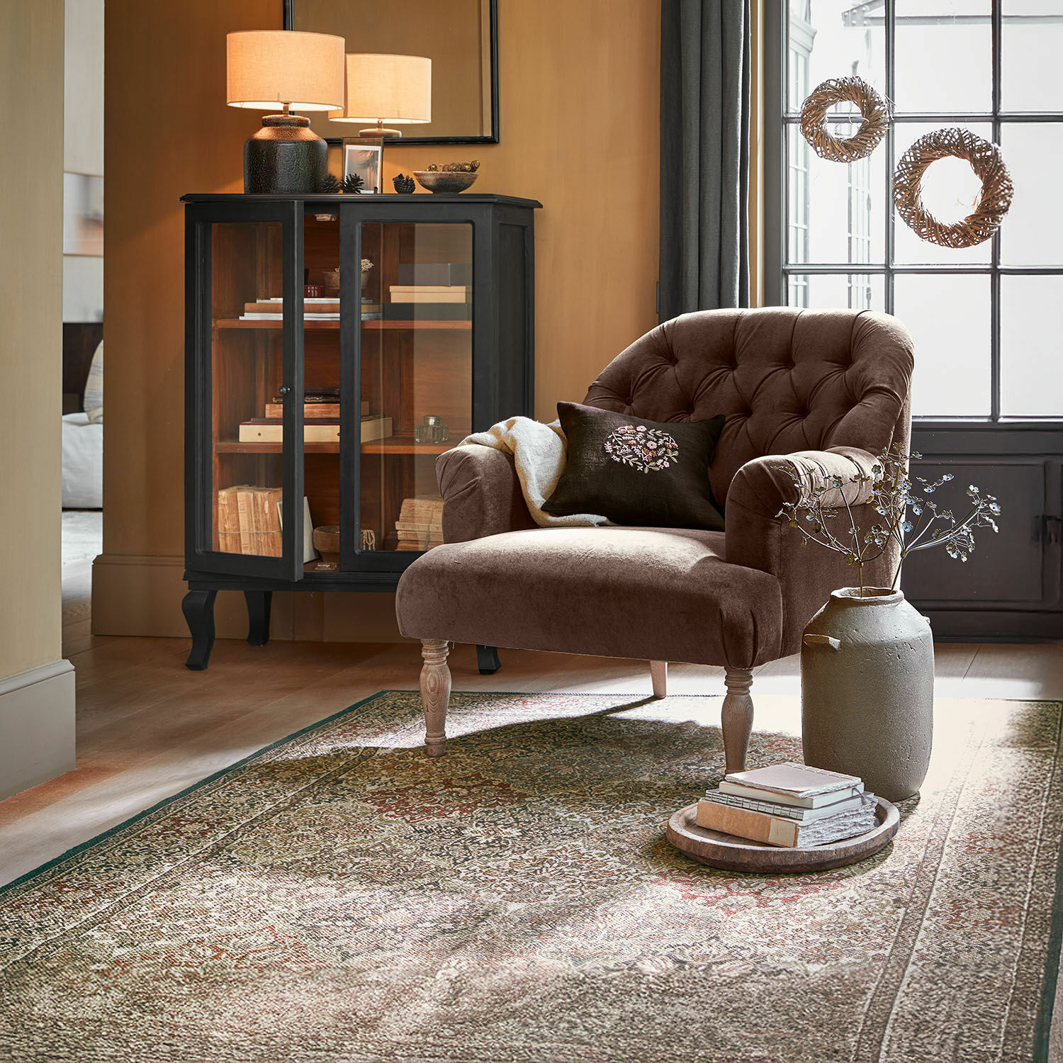 Vloerkleed voor binnen en buiten Malhira Bruine fluwelen fauteuil met gestikte rugleuning en houten poten in gezellige woonkamer met vloerkleed
