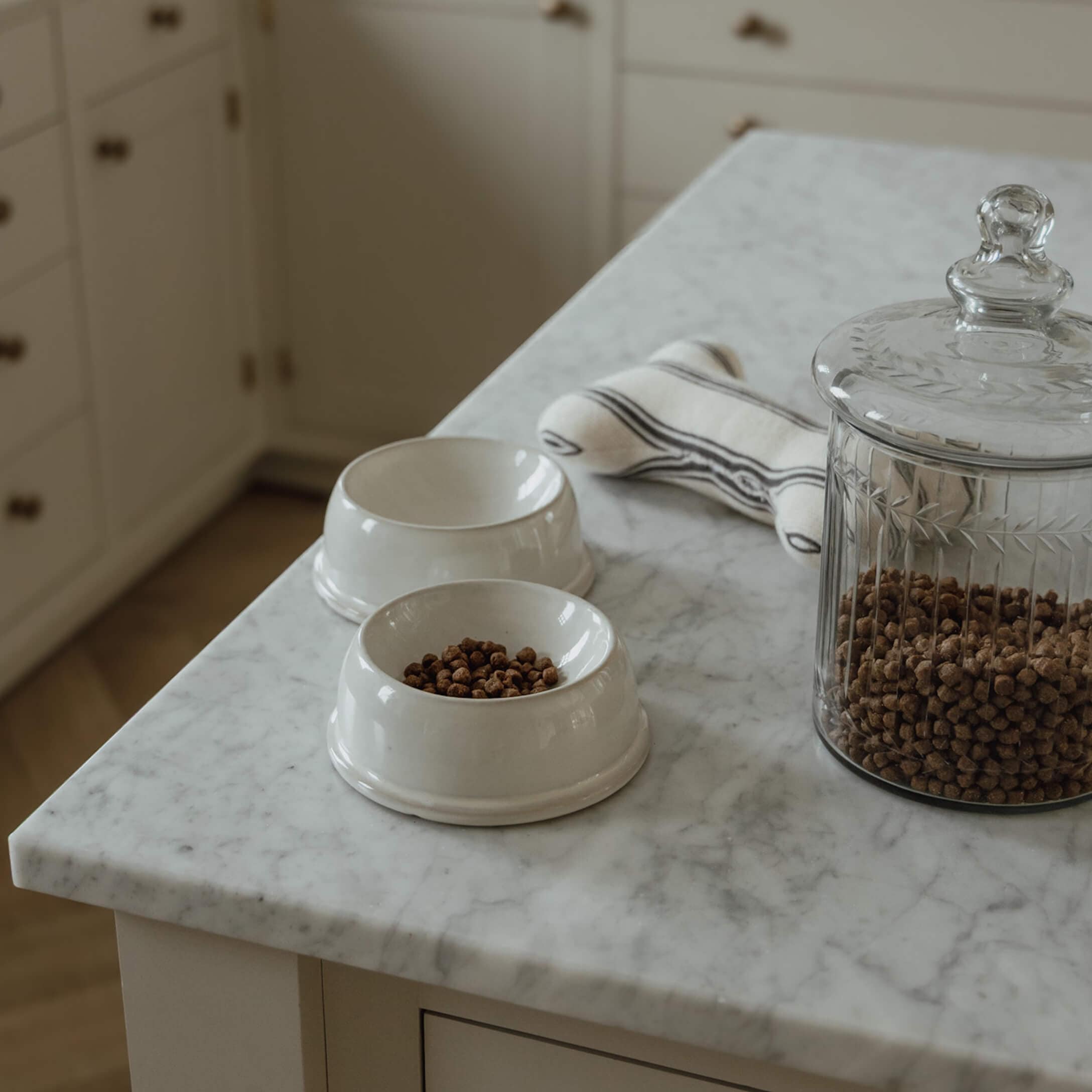 Witte keramische voerbakken met droogvoer en glazen pot op een marmeren keukenblad