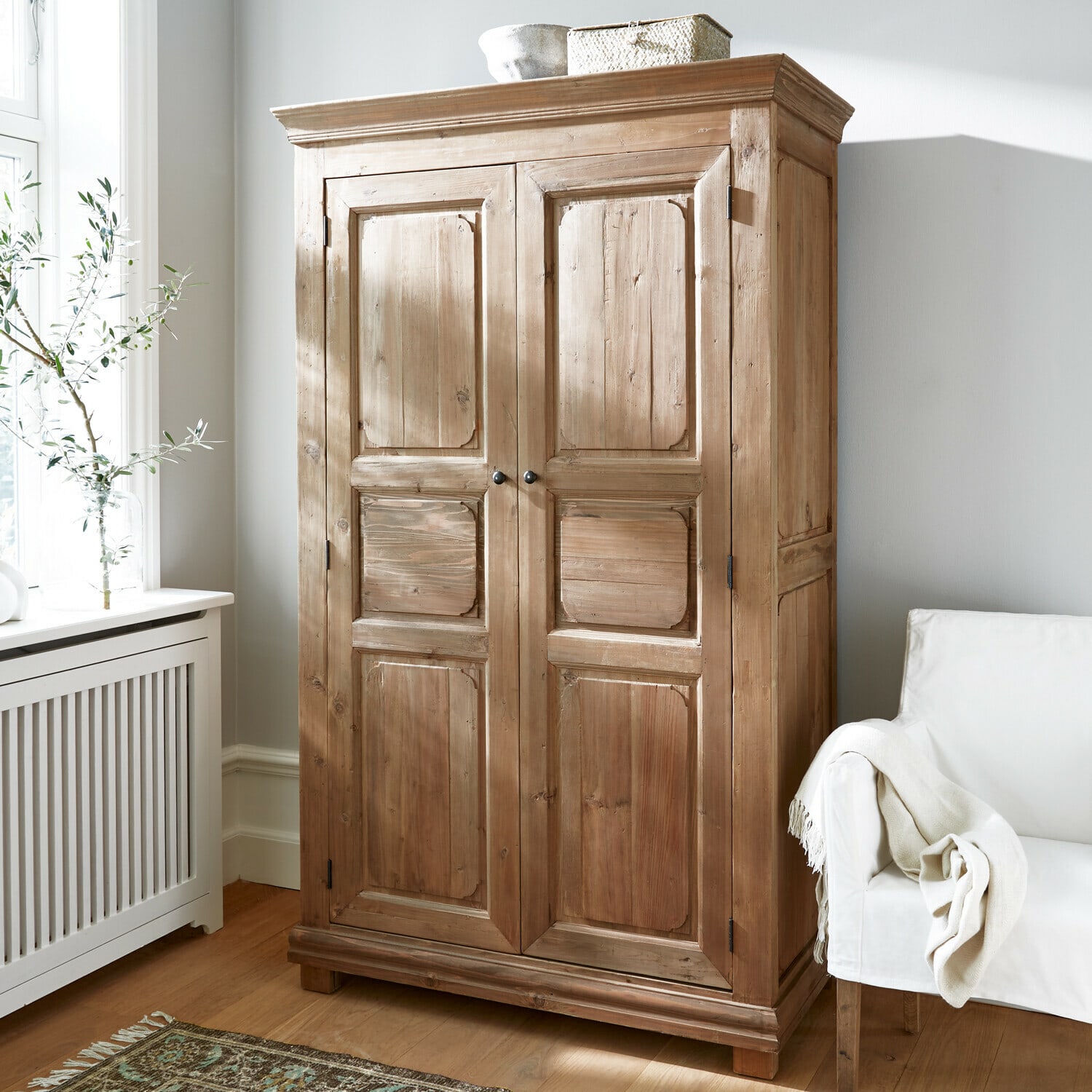 Kledingkast Gavrielle Houten kast in natuurlijke kleur in lichte kamer met witte stoel en patroon vloerkleed