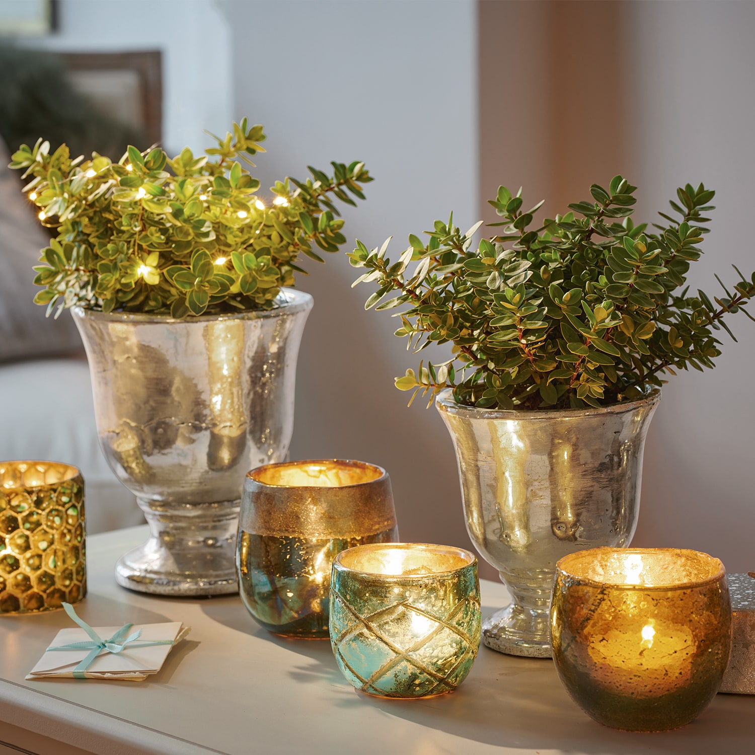 Decoratieve zilveren plantenbakken met groene planten en glazen theelichthouders met warm licht op tafel