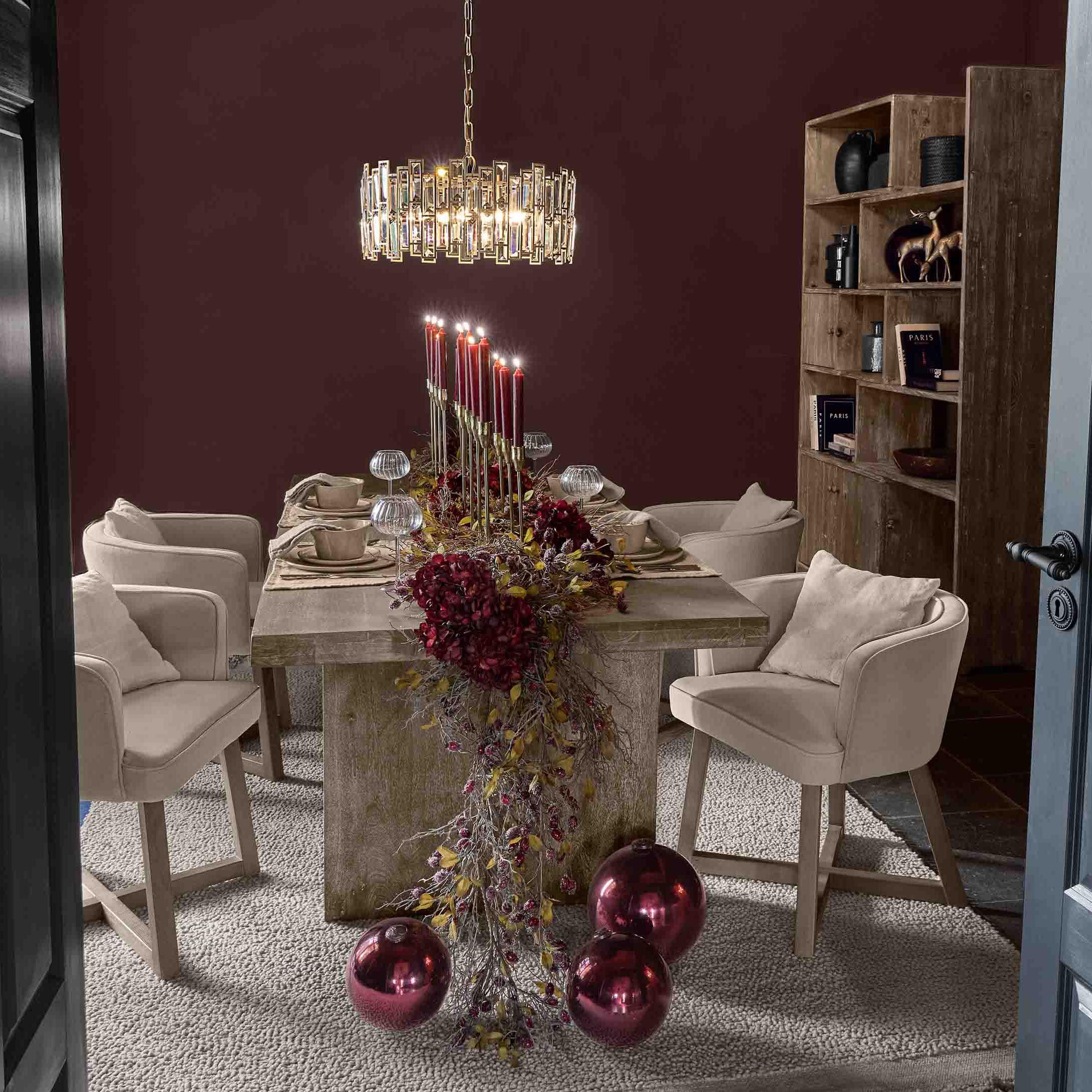 Eetkamer met houten tafel, beige stoelen en decoratie van rode kaarsen en glanzende kerstballen