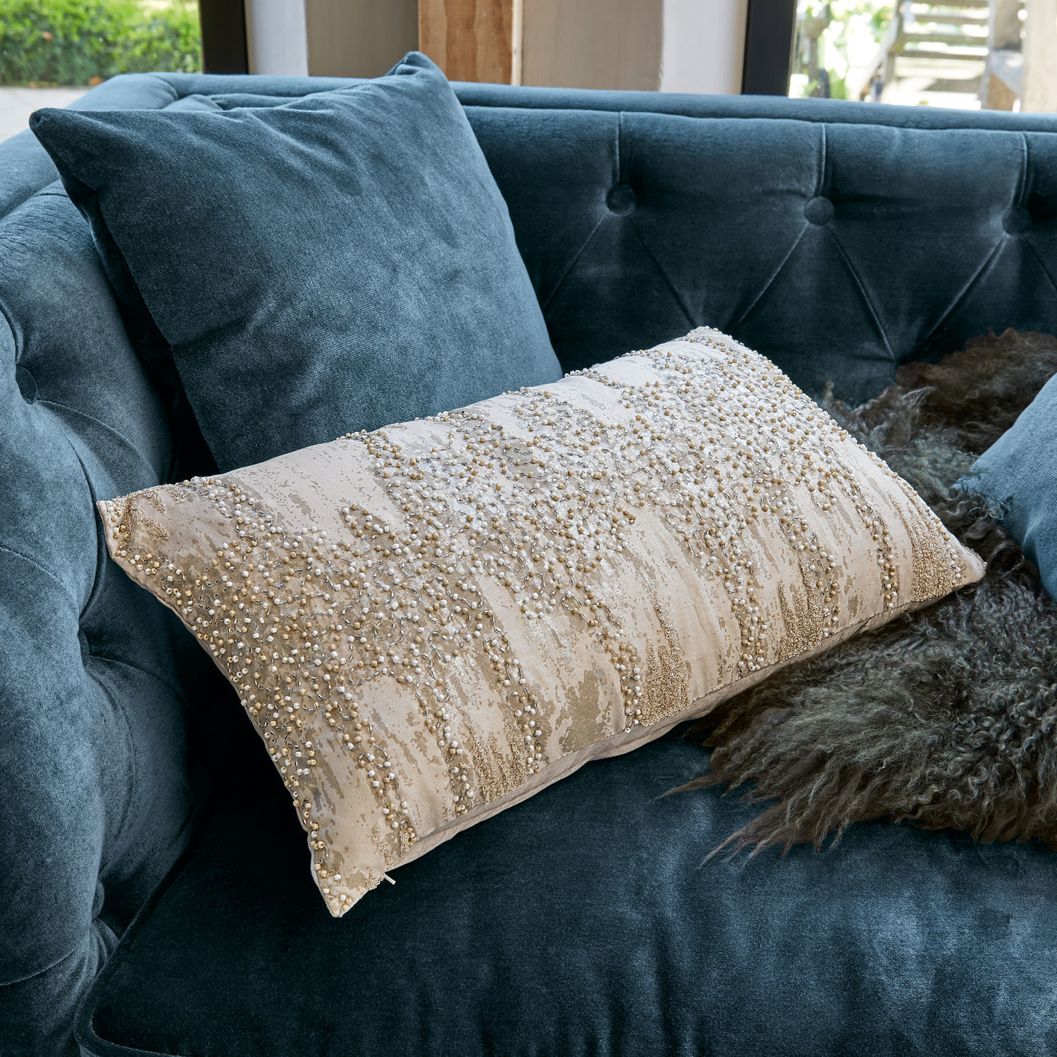 Beige sierkussen met kralen op blauwe fluwelen bank, stijlvolle woonaccessoire