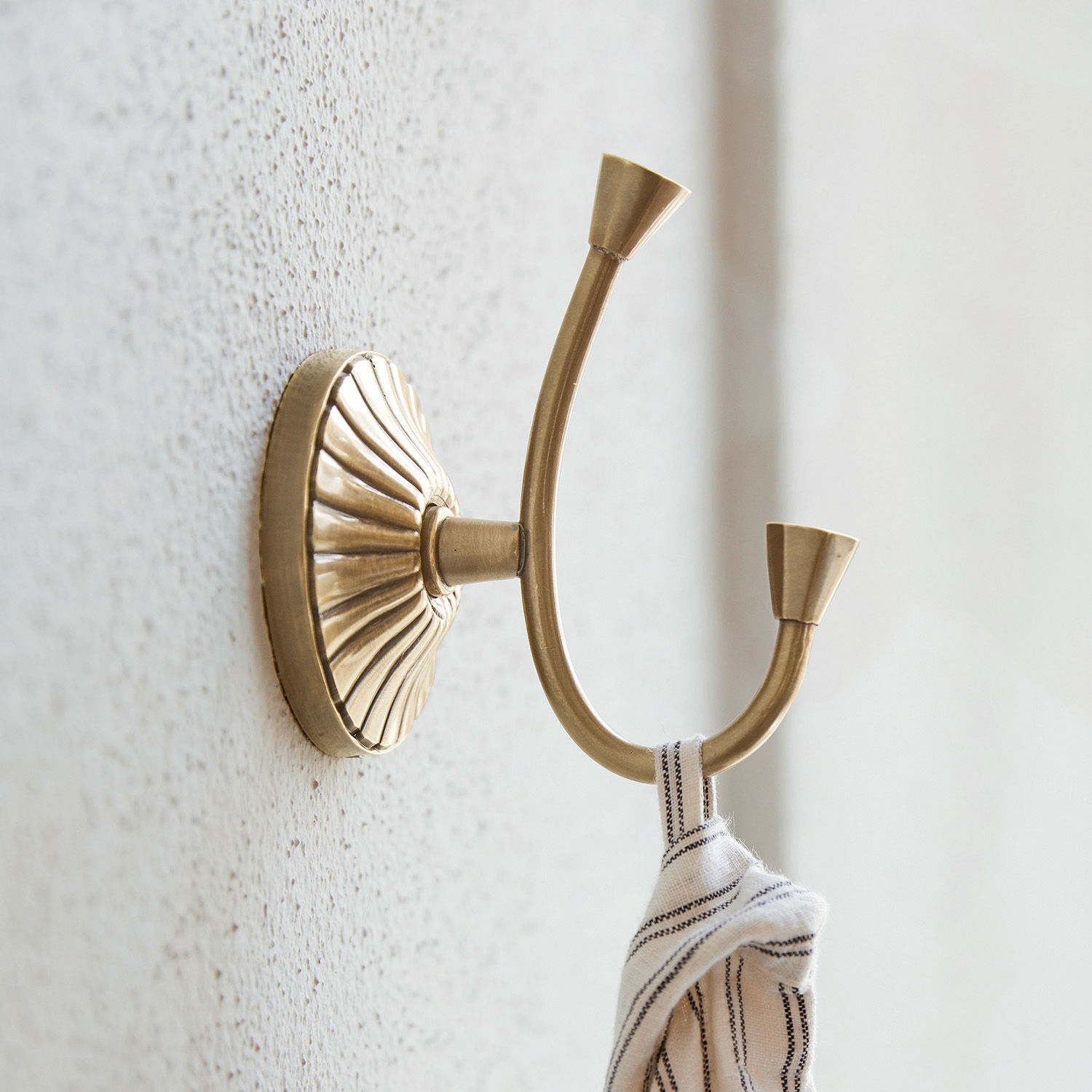 Haak Terling Dubbele messing wandhaak met decoratieve basis en opgehangen stof, vintage stijl