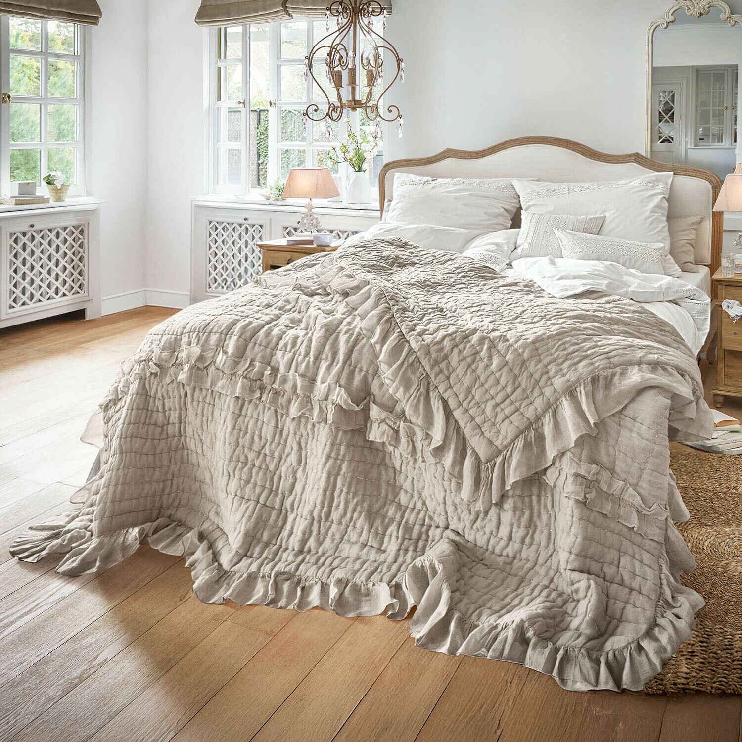 Beige bedsprei met ruches van zachte stof op bed in lichte slaapkamer met houten vloer