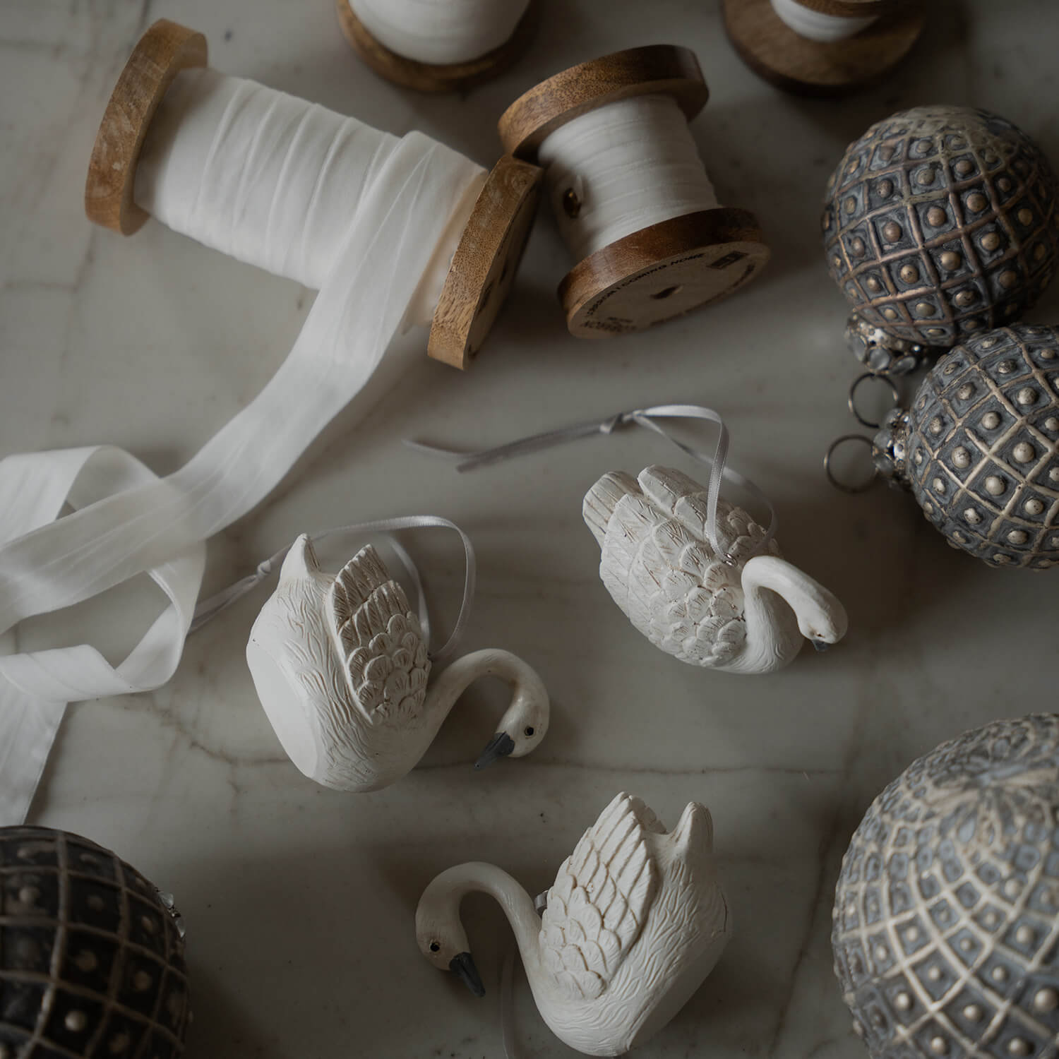 Witte keramische zwaanornamenten met lint en houten spoelen met wit lint op marmeren tafel