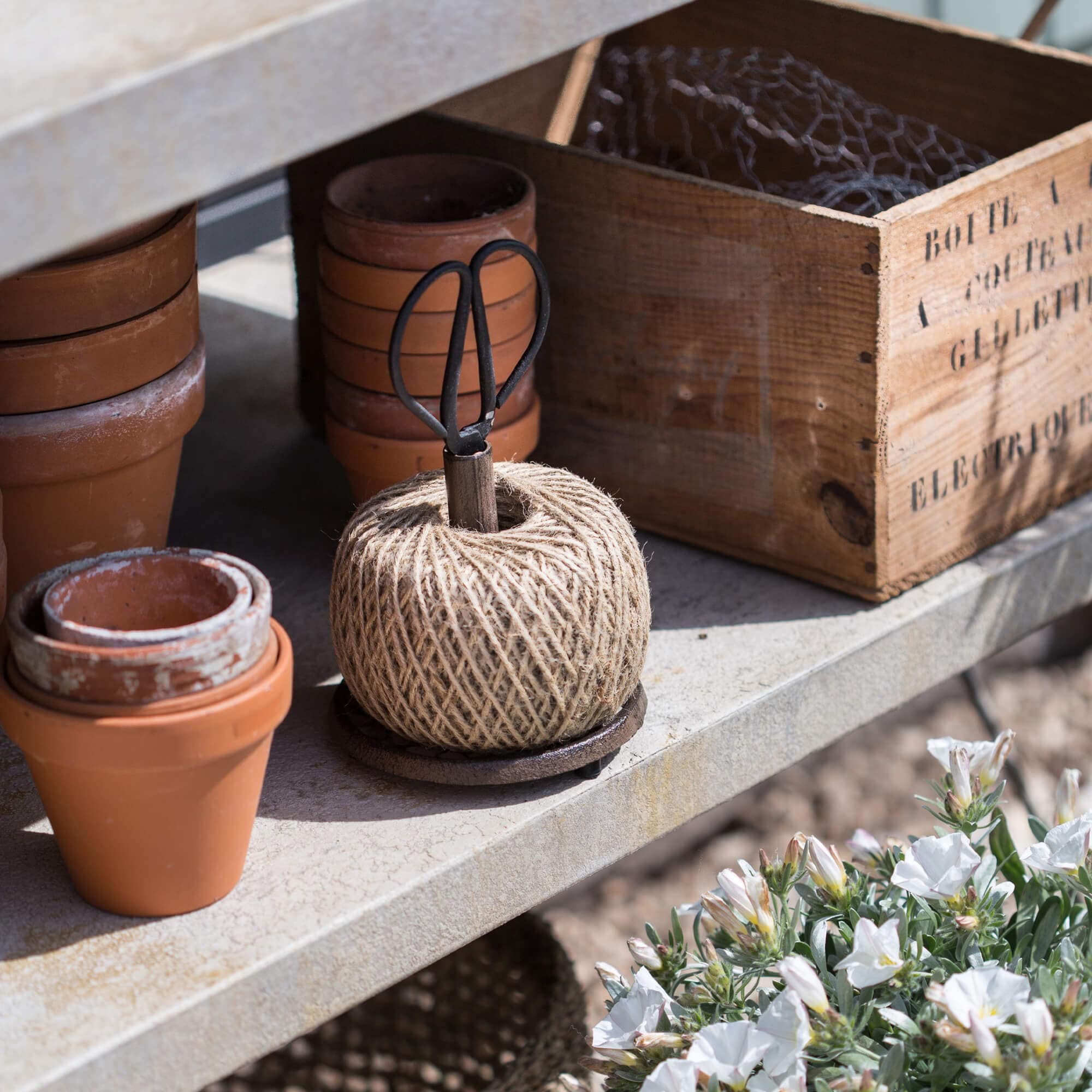 Natuurlijke tuindraad met metalen schaar op betonnen plank naast terracotta potten en houten kist