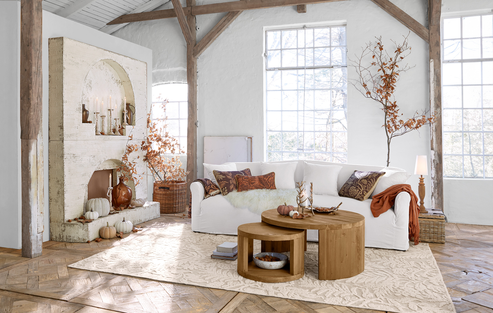 Gezellige landelijke woonkamer met witte bank, ronde houten tafels en herfstdecoratie in warme bruine tinten