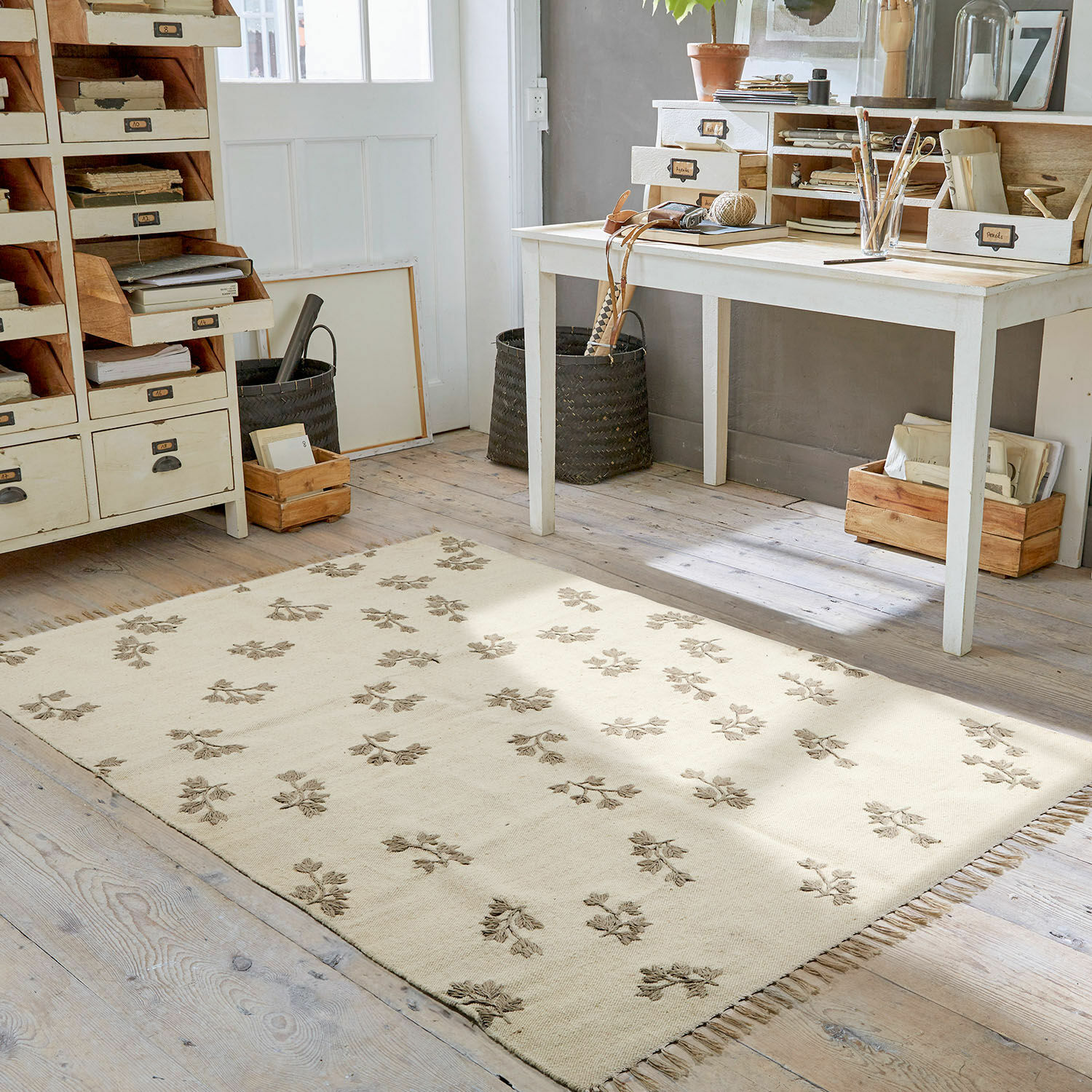Beige vloerkleed met bloemenpatroon en franjes op houten vloer in lichte werkkamer