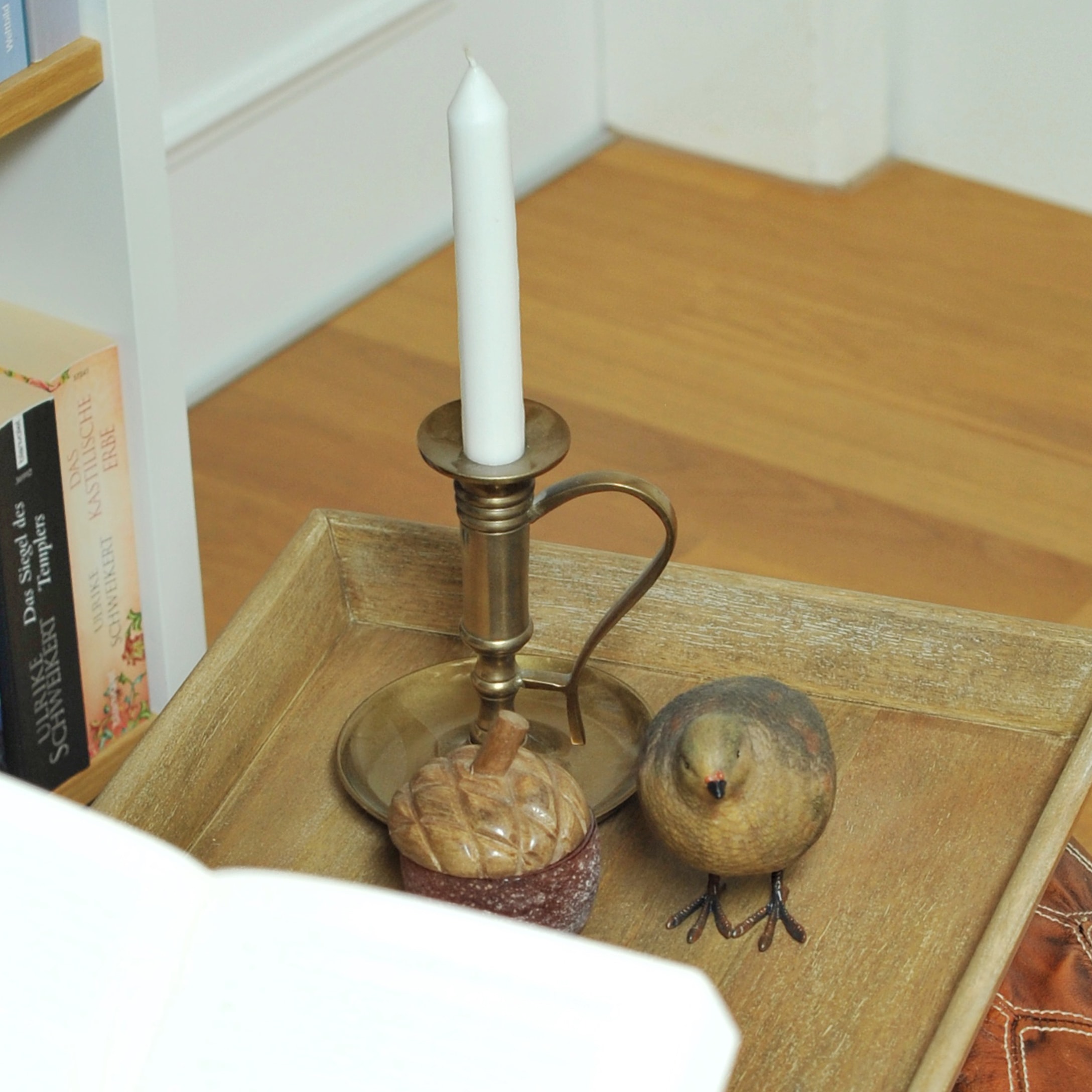 Messing kandelaar met witte kaars en decoratieve vogel op houten dienblad in woonkamer