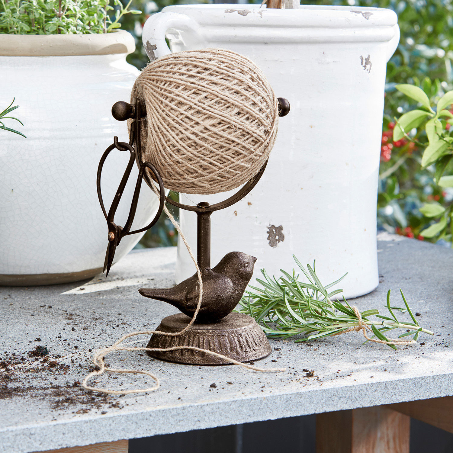 Bruine metalen houder met garenbol, schaar en vogelornament op tuintafel van steen