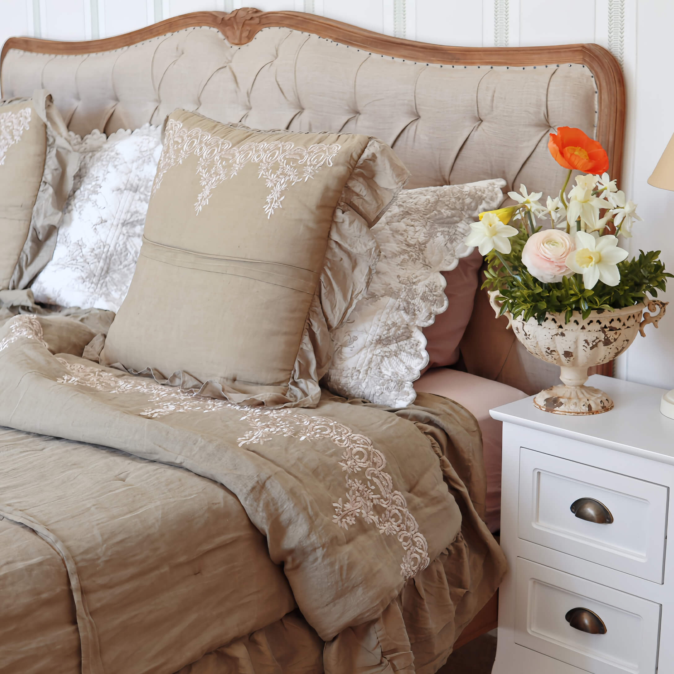 Beige beddengoed met geborduurde kussens en deken op bed met gestoffeerd hoofdeinde