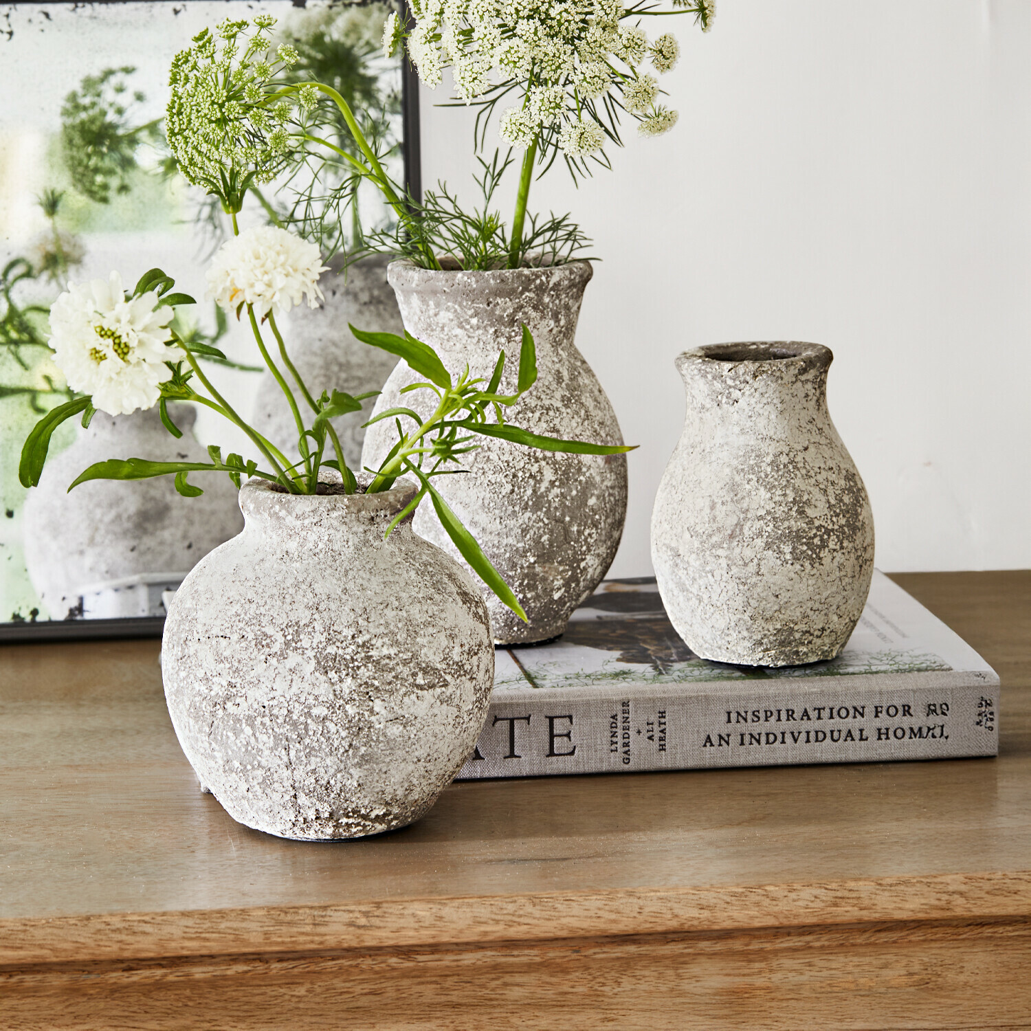 Drie rustieke stenen vazen in grijs-wit op houten tafel met witte bloemen