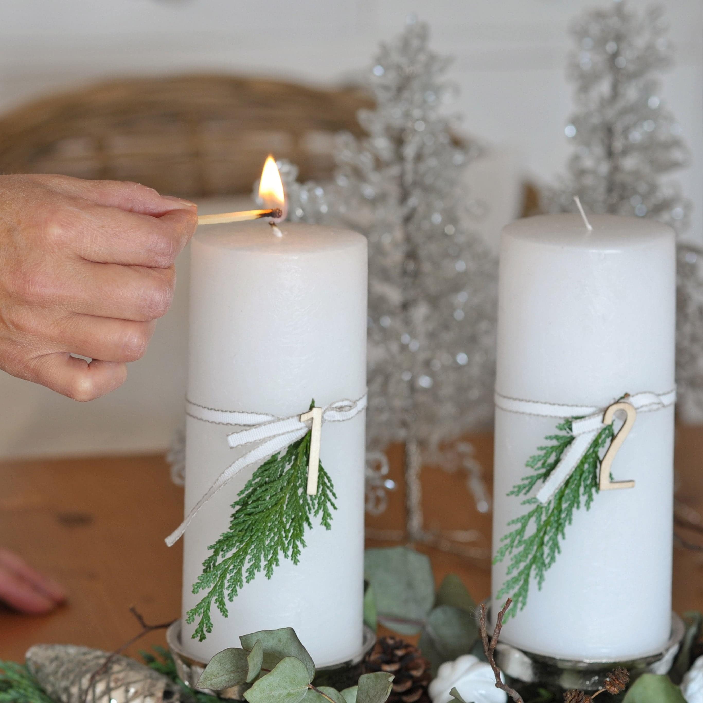 Witte adventskaarsen met groene takken en houten nummers op een decoratief kerstplateau