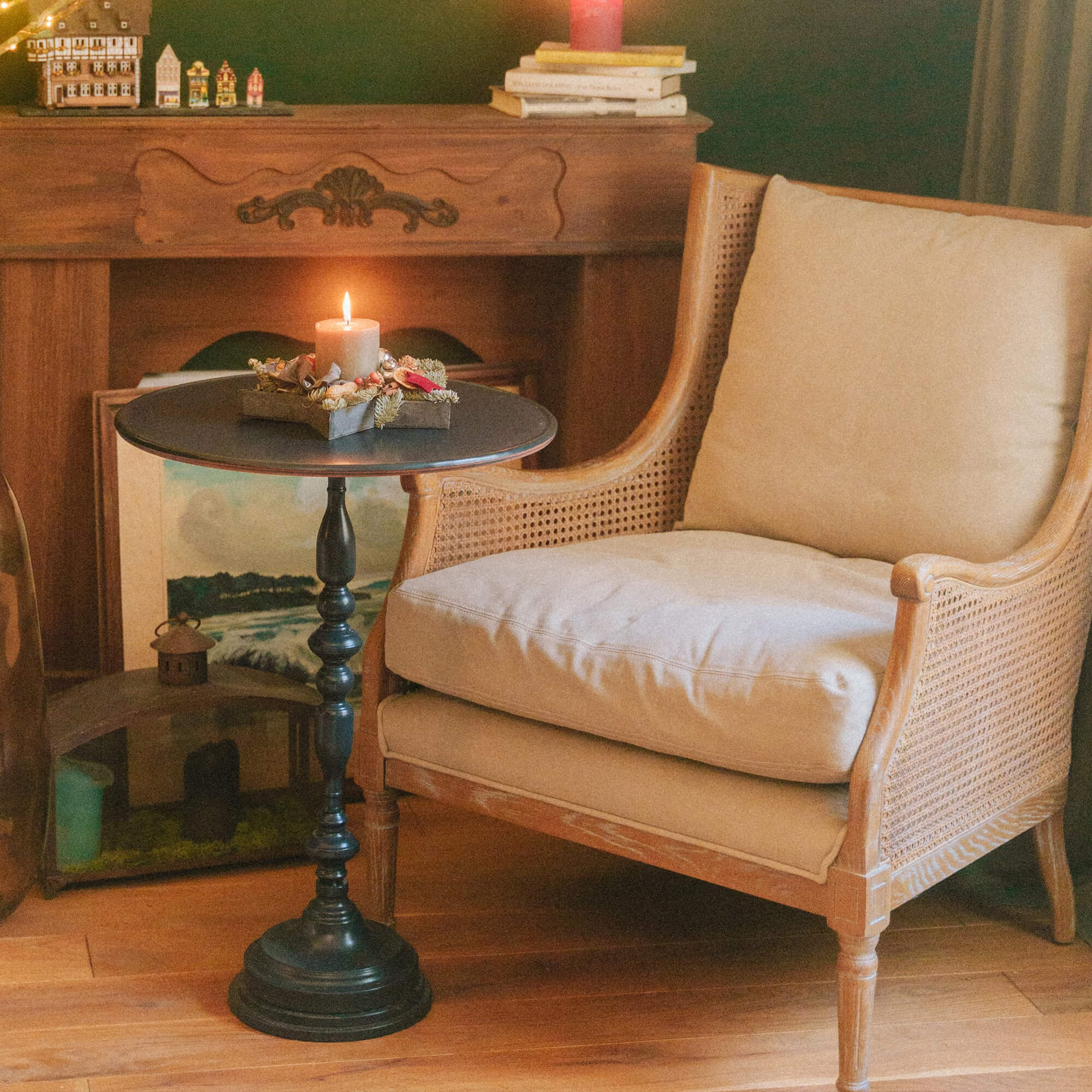 Beige houten fauteuil met kussen en zwarte bijzettafel met kaars in gezellige kamer