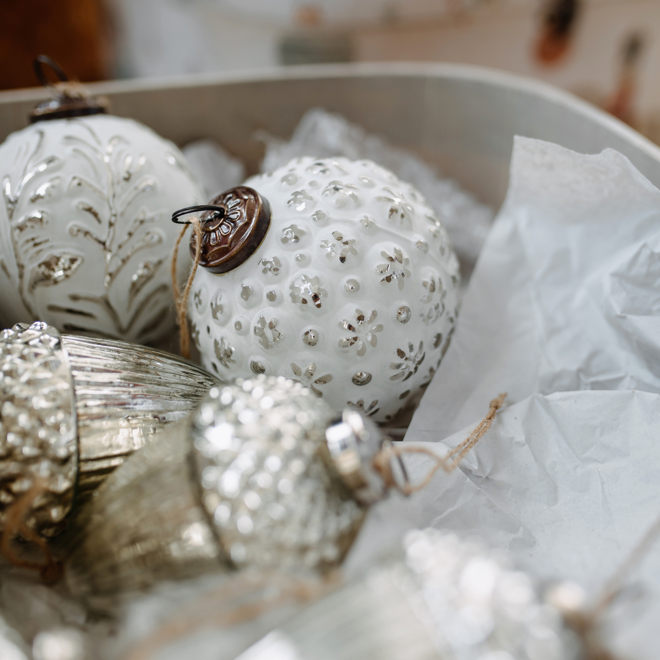 Witte en zilveren kerstballen van glas en metaal met patronen, in doos met papier