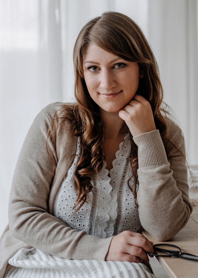 Vrouw in beige trui en witte kanten blouse zittend aan tafel met een schaar