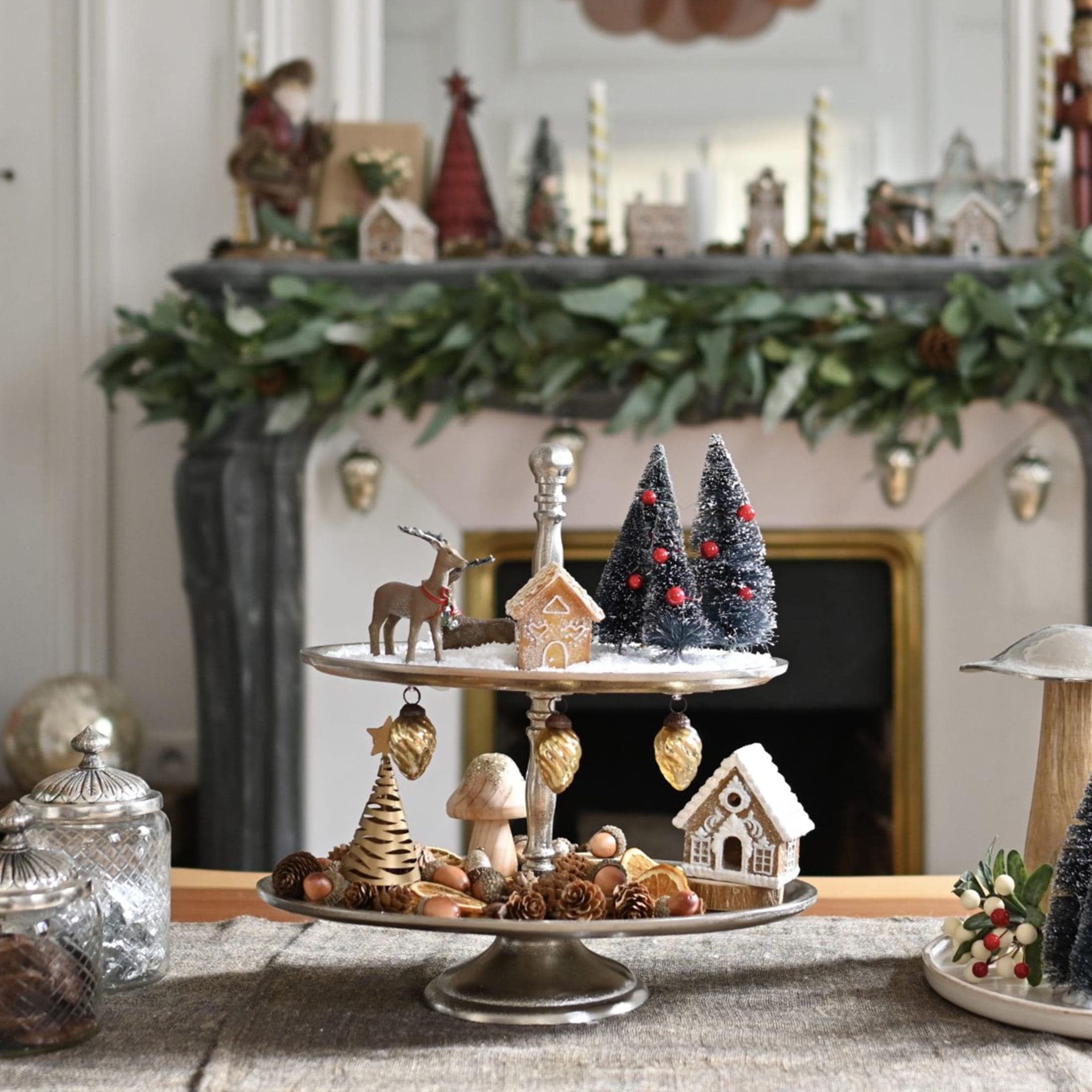 Twee verdiepingen metalen etagère met kerstdecoraties en peperkoekhuisjes op tafel