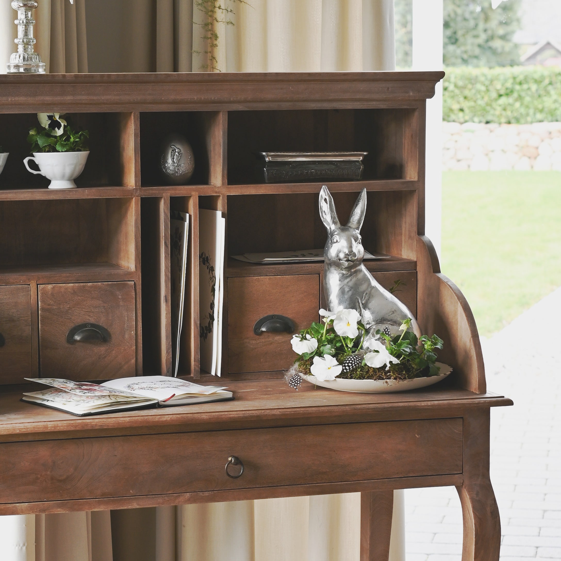 Houten bureau met laden en zilveren konijndecoratie met witte bloemen op een bord