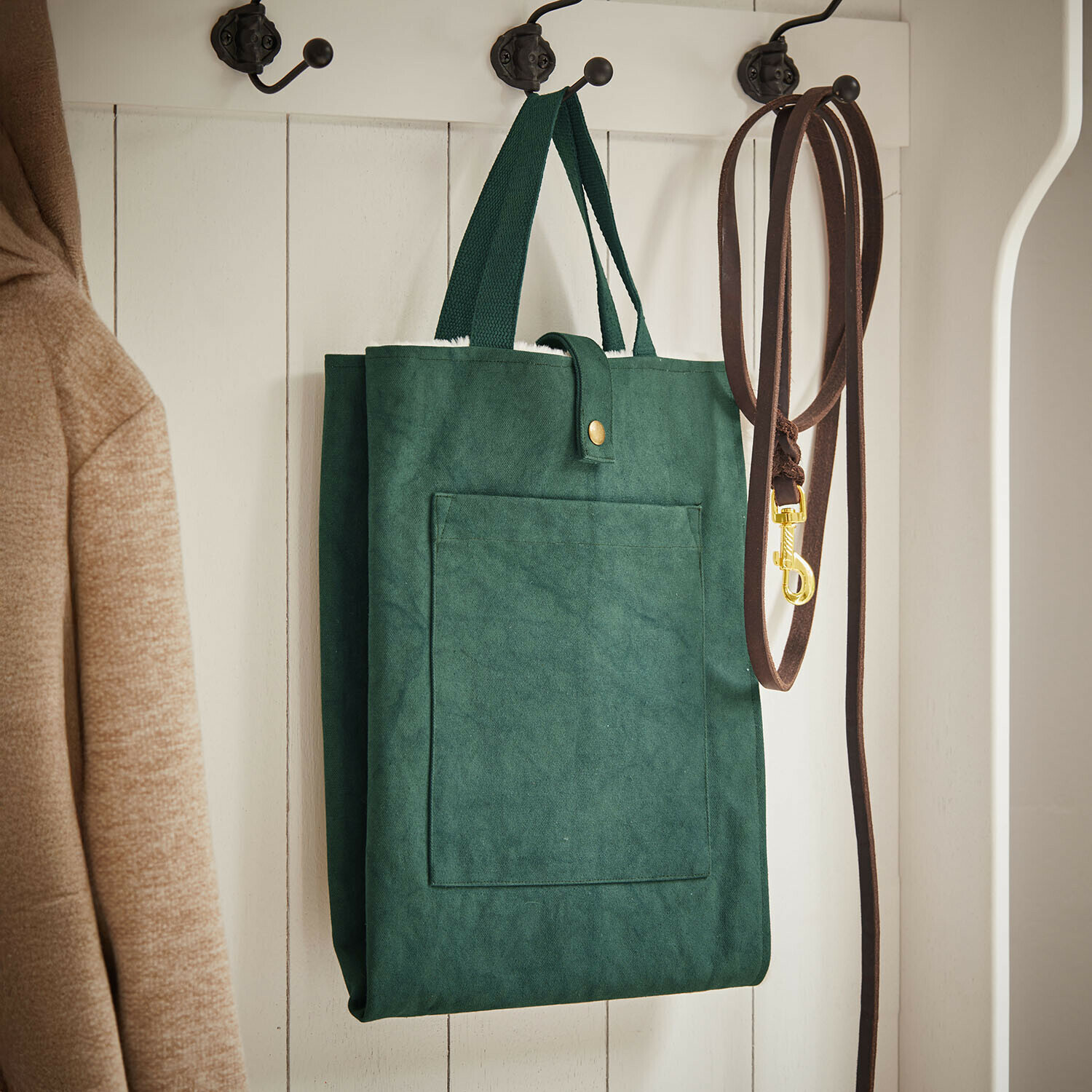Huisdierenmat Felliro Groene stoffen tas hangend aan witte houten kapstok naast bruine riem en beige jas