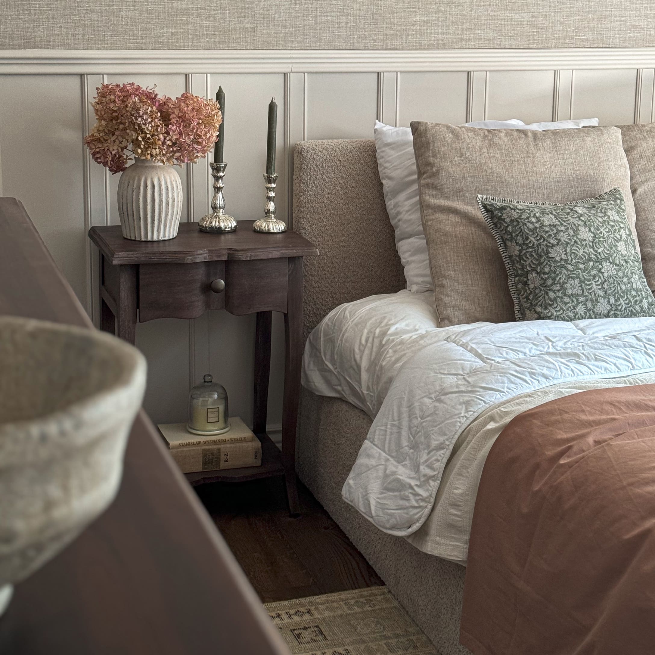 Gezellige slaapkamer met beige beddengoed, houten nachtkastje en decoratieve vaas met gedroogde bloemen