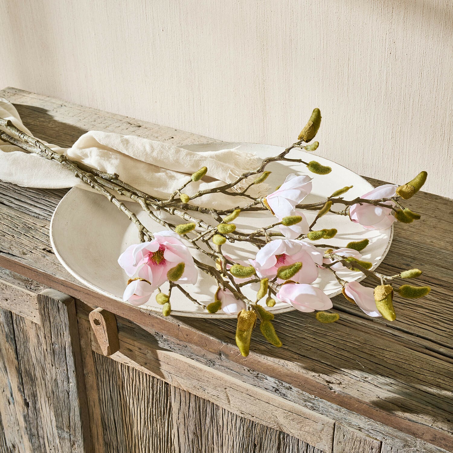 Magnoliatakken met roze bloemen en groene knoppen op een wit bord op een rustieke houten tafel