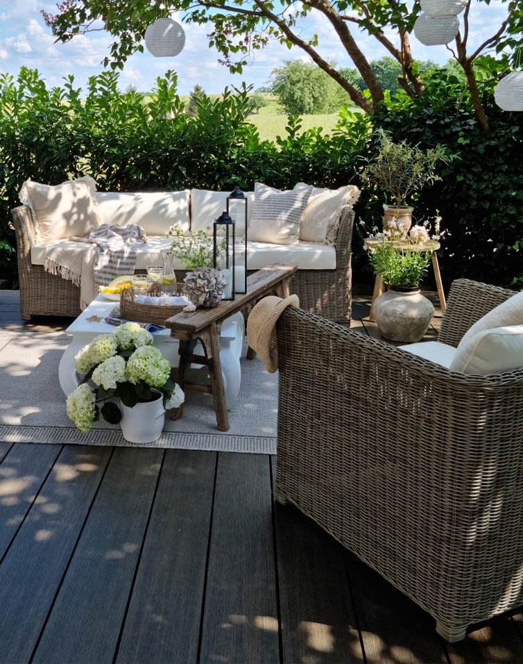 Gezellige tuinmeubelen van riet met beige kussens op terras met bloemen en lantaarns