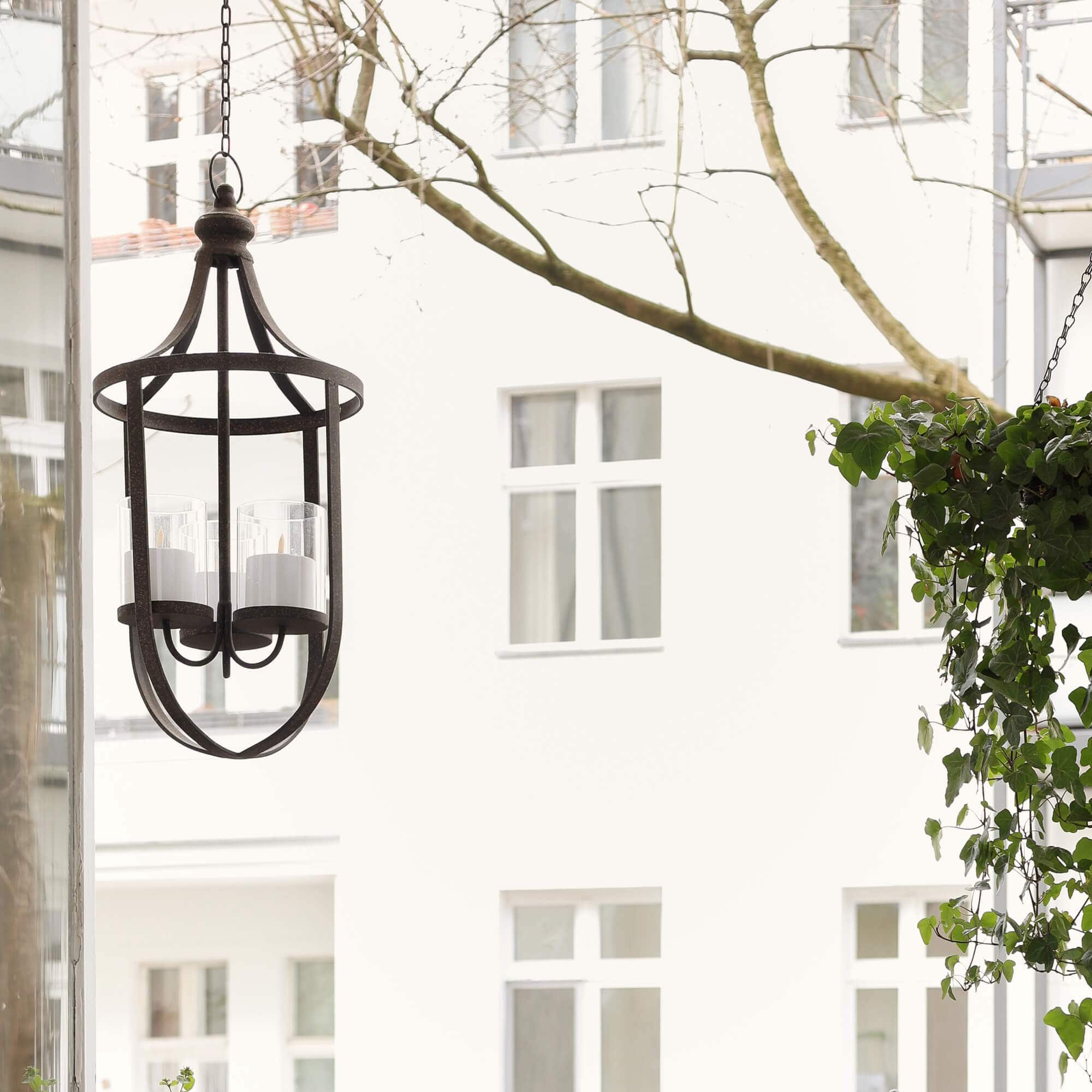 Hangende metalen lantaarn met drie witte kaarsen voor ramen en groen balkonplanten