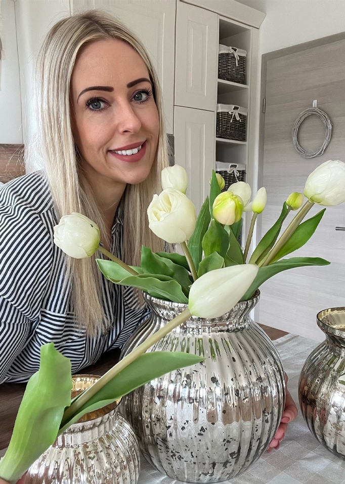 Vrouw met blond haar naast zilveren vaas met witte tulpen in modern interieur