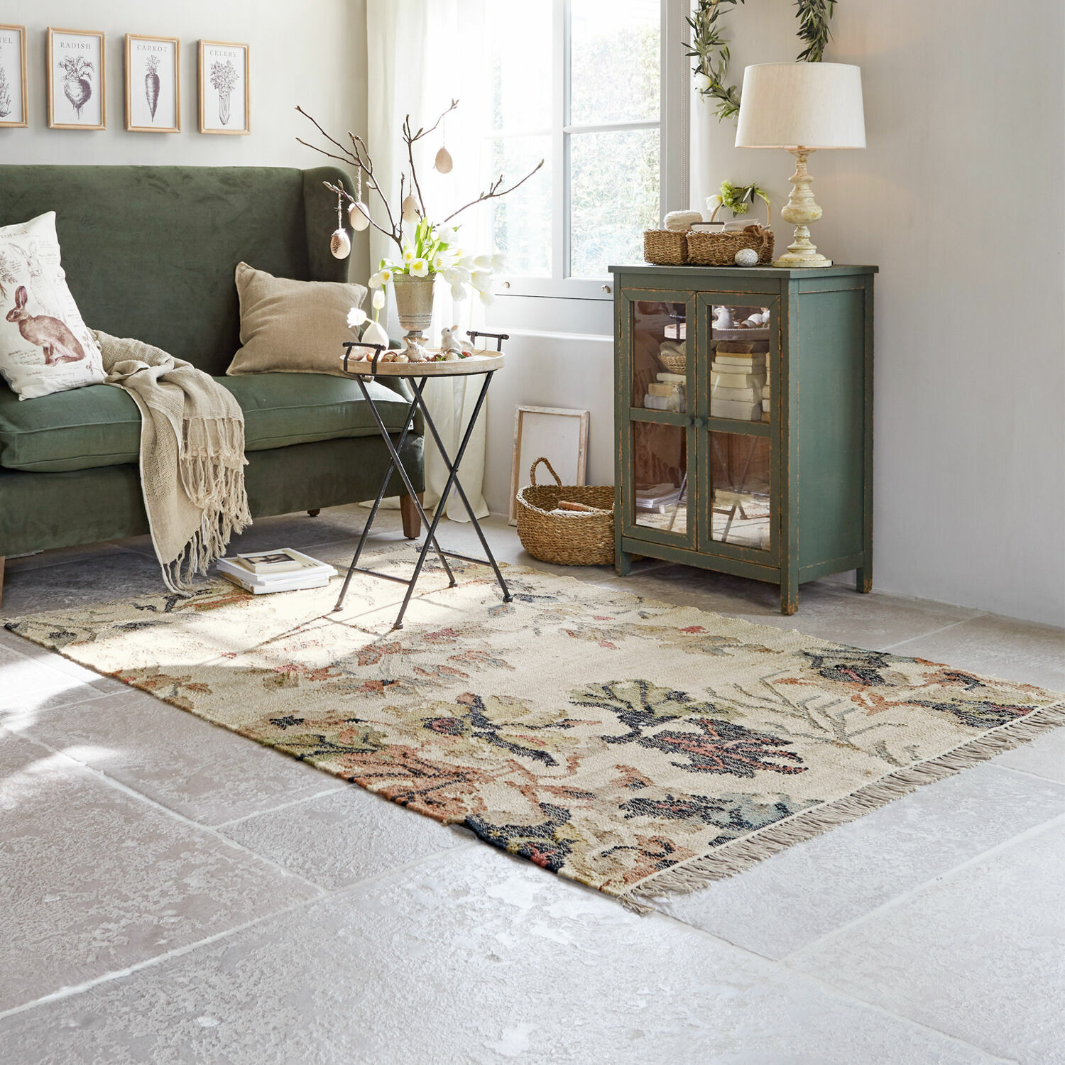 Gezellige woonkamer met groene bank, beige vloerkleed met bloemenpatroon en vintage houten kast