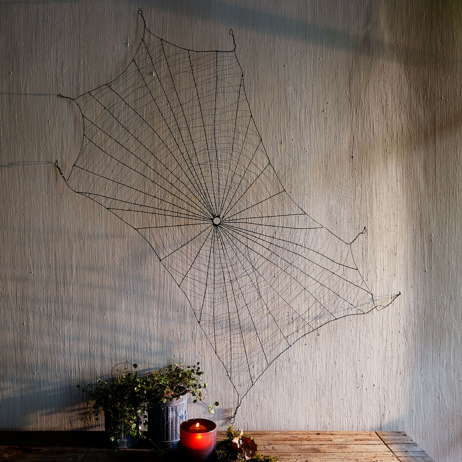 Decoratief spinnenweb Vexilnor Zwarte metalen spinnenweb wanddecoratie met rode kaars en plant op houten tafel
