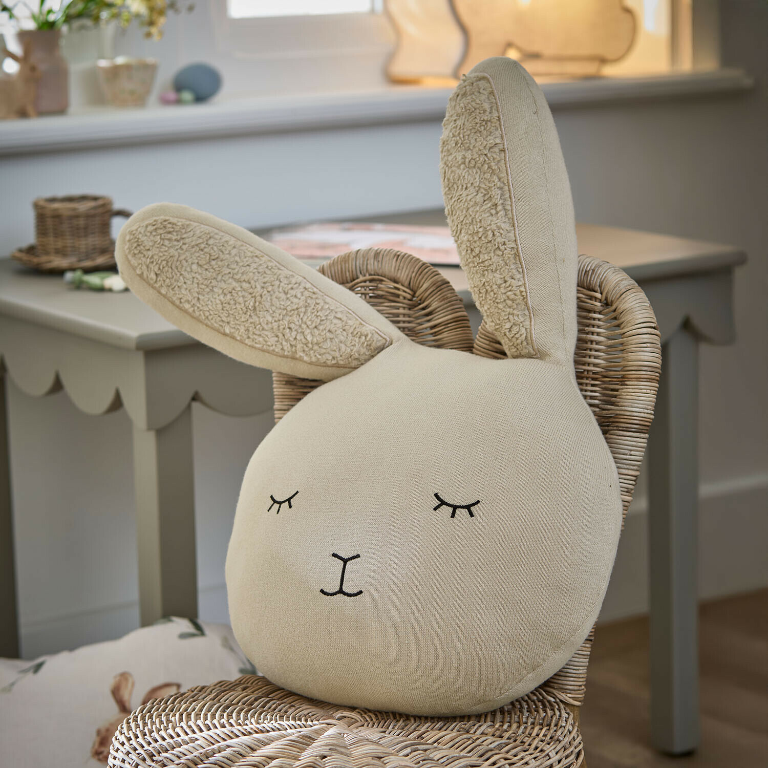 Beige konijnenkussen van zachte stof op een rotan stoel in een kinderkamer