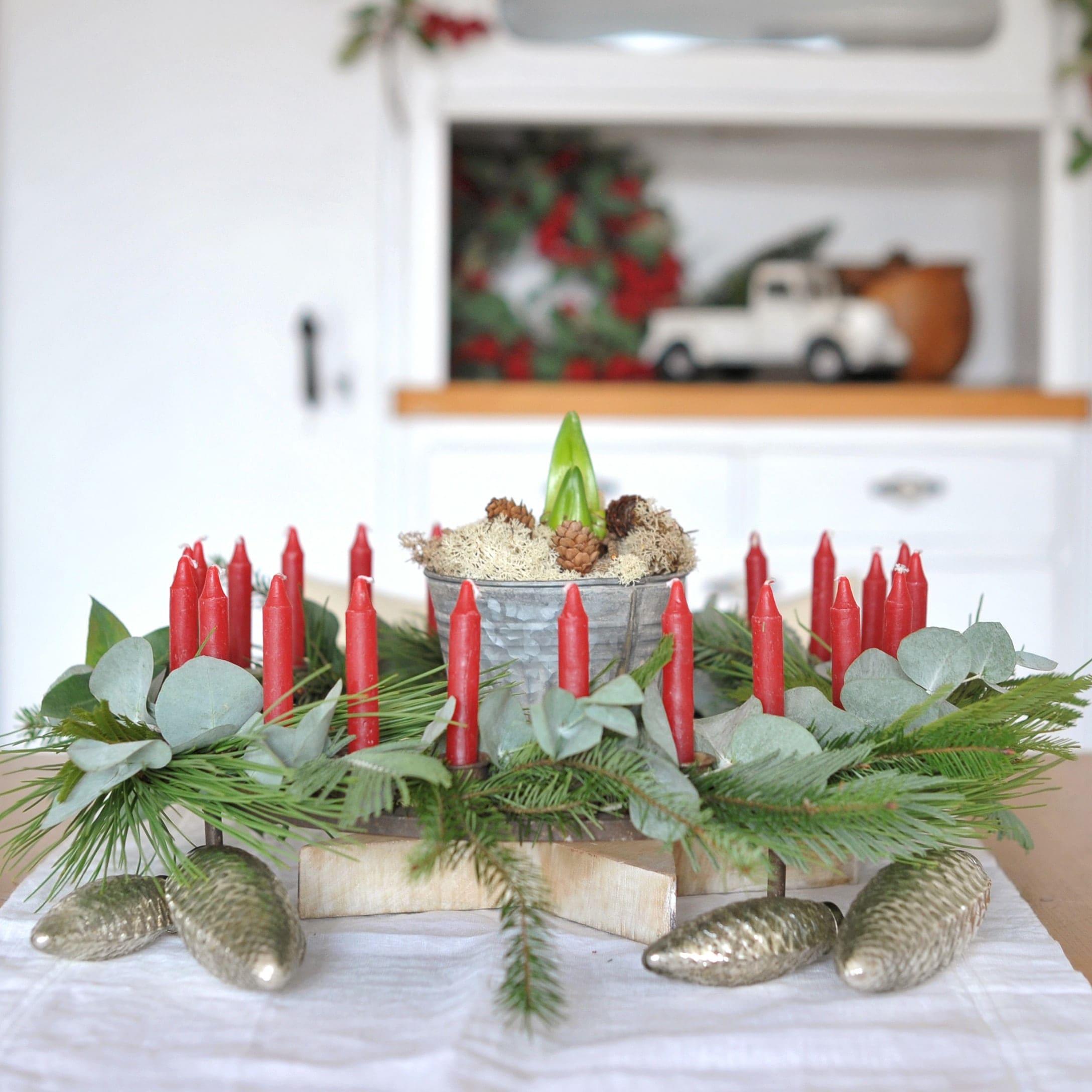 Decoratieve adventskrans met rode kaarsen, groene takken en metalen dennenappels op tafel