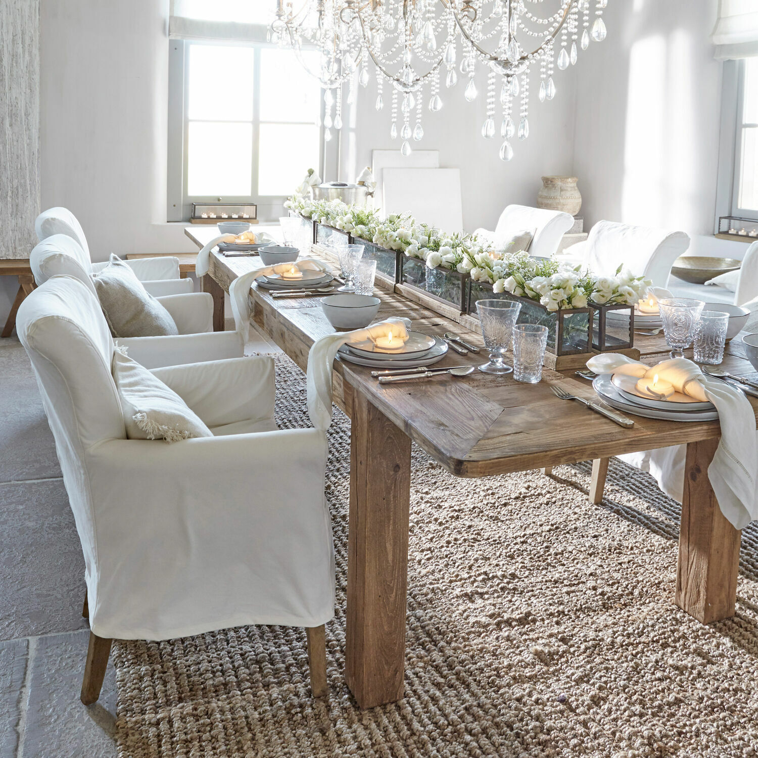 Eetkamer met houten tafel en witte beklede stoelen, bloemen en kaarsen als decoratie