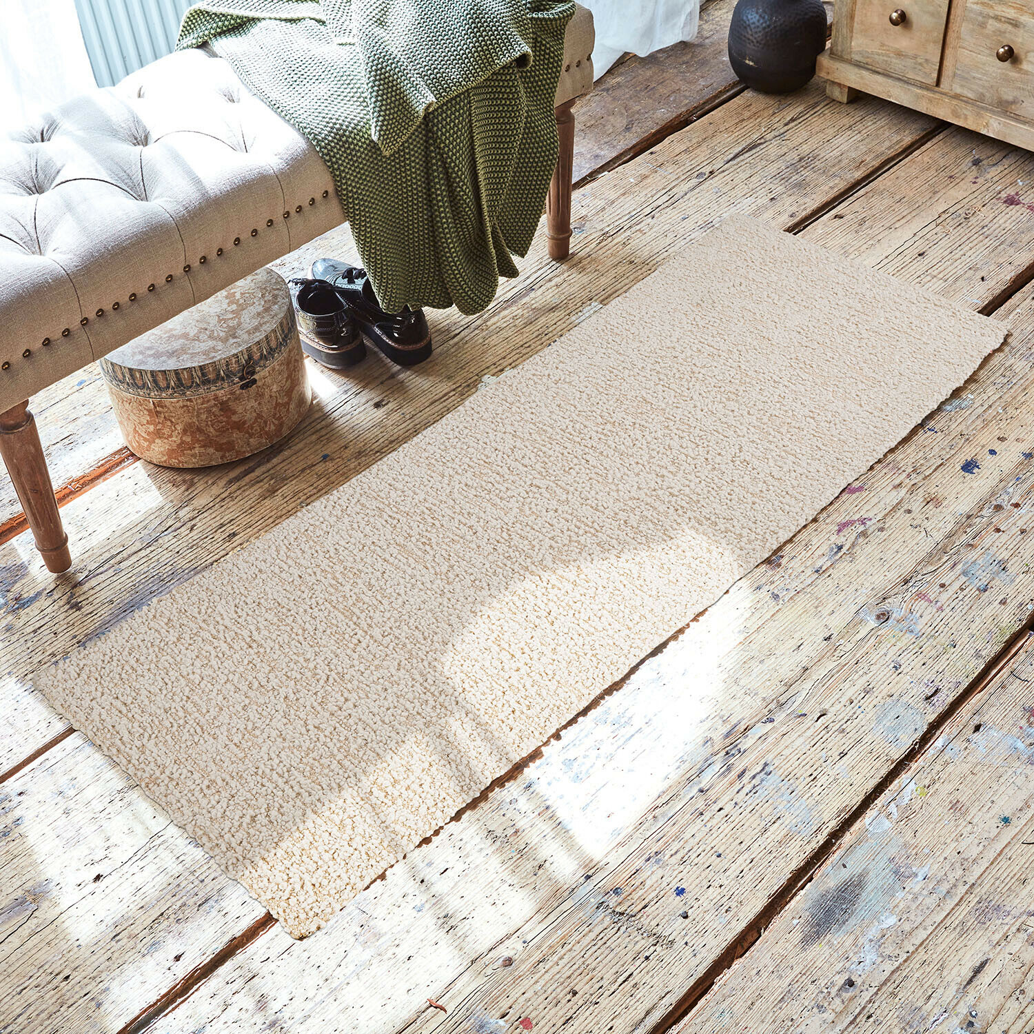 Beige vloerkleed van zacht materiaal op houten vloer in gezellige ruimte met bank en groene deken