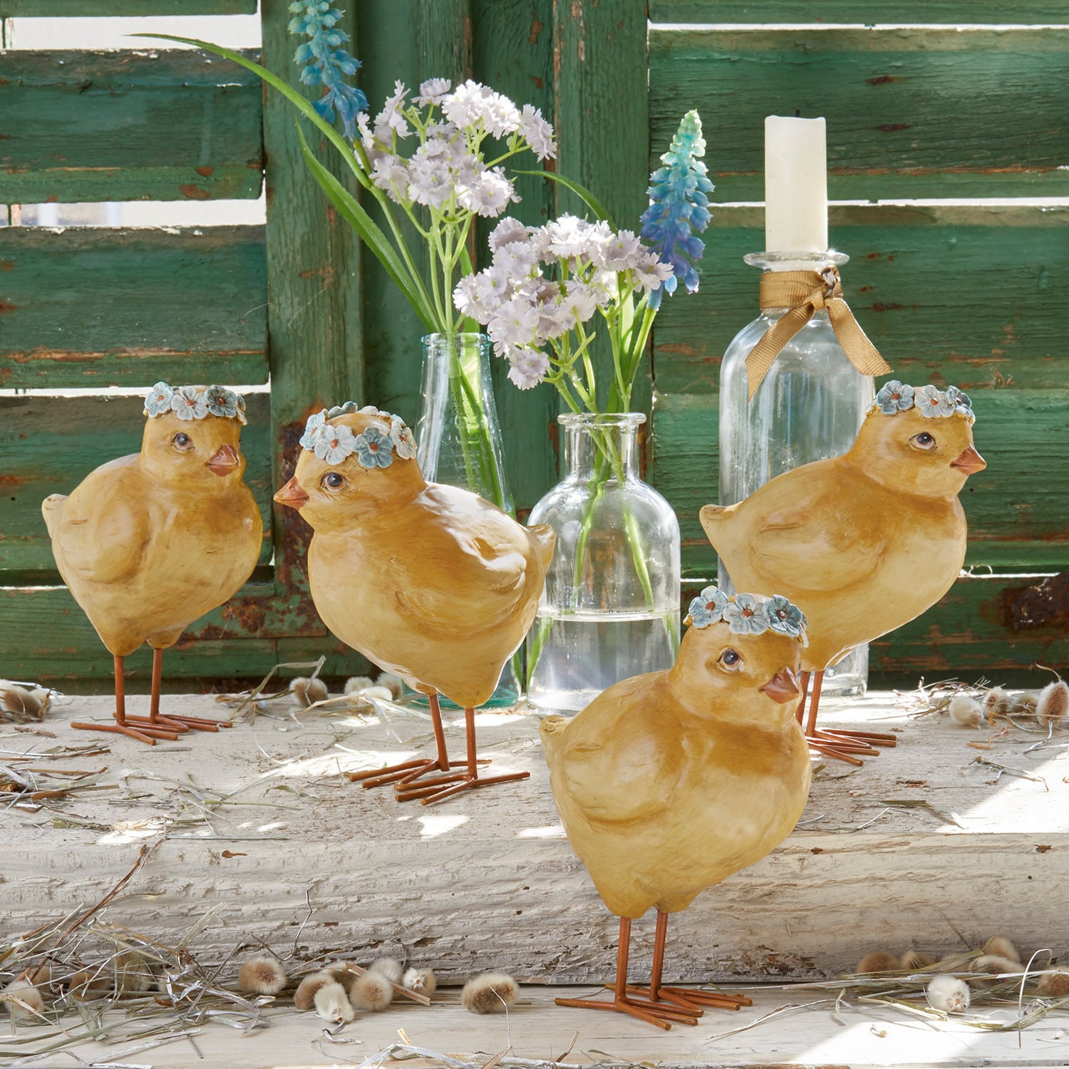 Vier gele decoratieve kuikens van materiaal met blauwe bloemenkransen voor een groene houten achtergrond