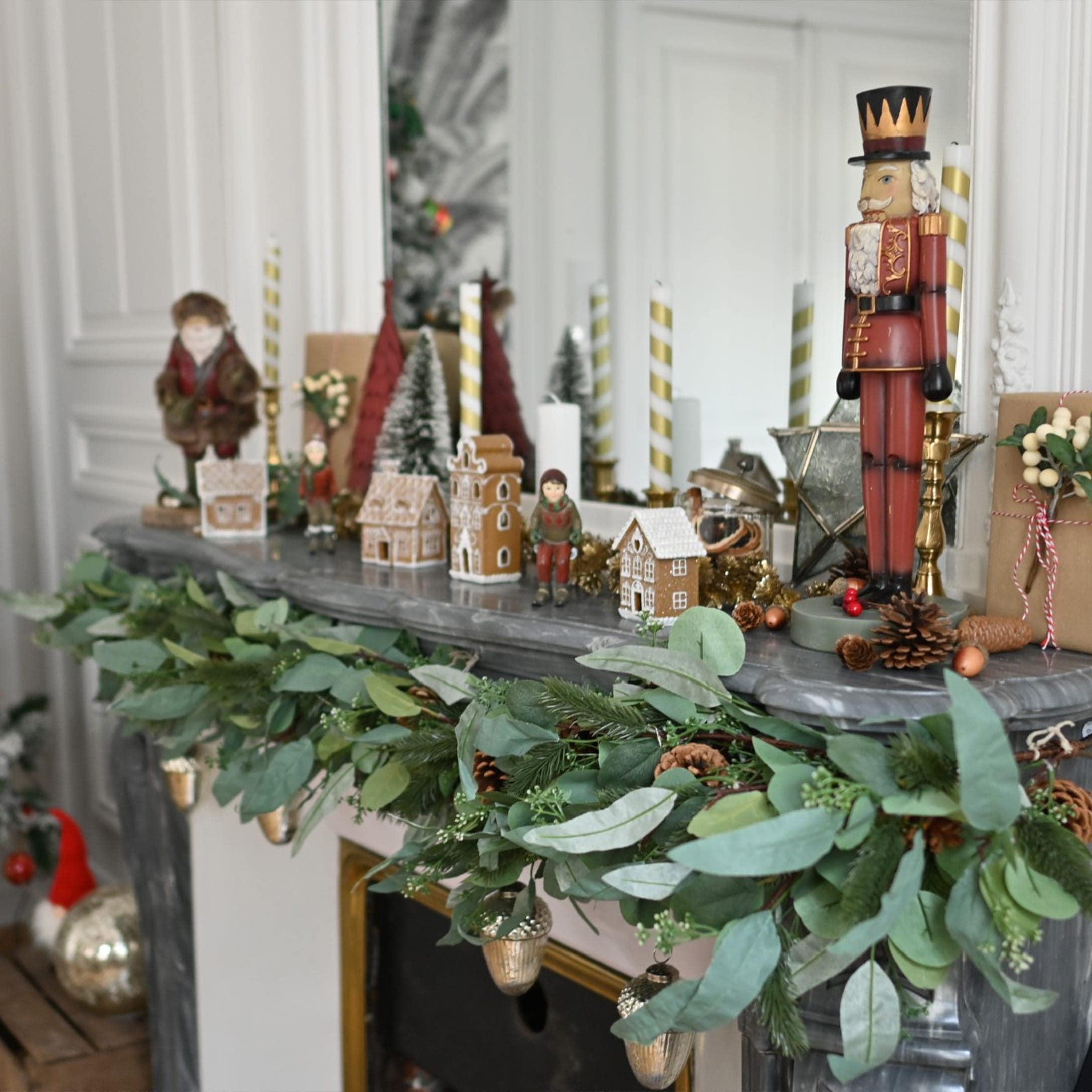 Kerstsfeer op schoorsteenmantel met groene takken, dennenappels en notenkrakerfiguur op grijs marmer