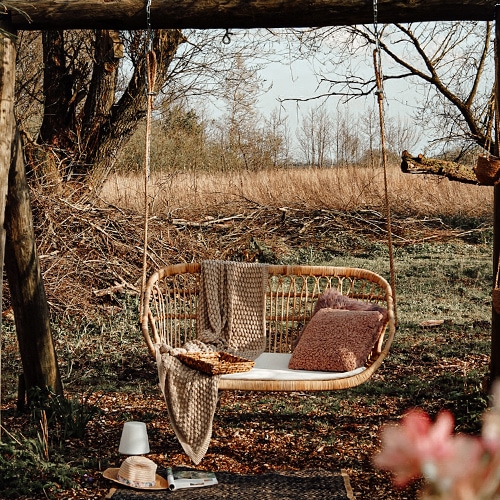 Rotan schommel in natuurlijke kleur met kussen en deken in een herfsttuin