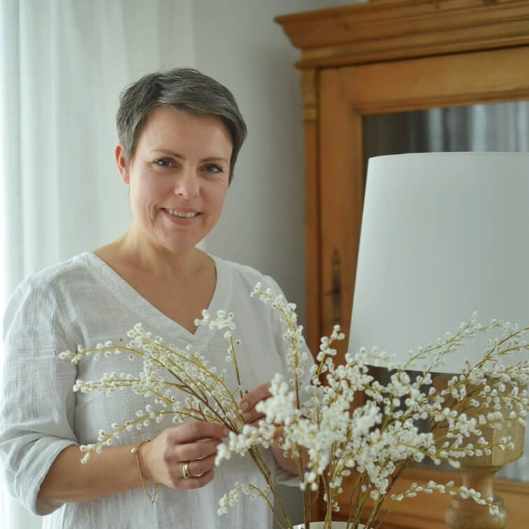 Vrouw in wit shirt houdt decoratieve takken met witte bloemen vast in lichte kamer