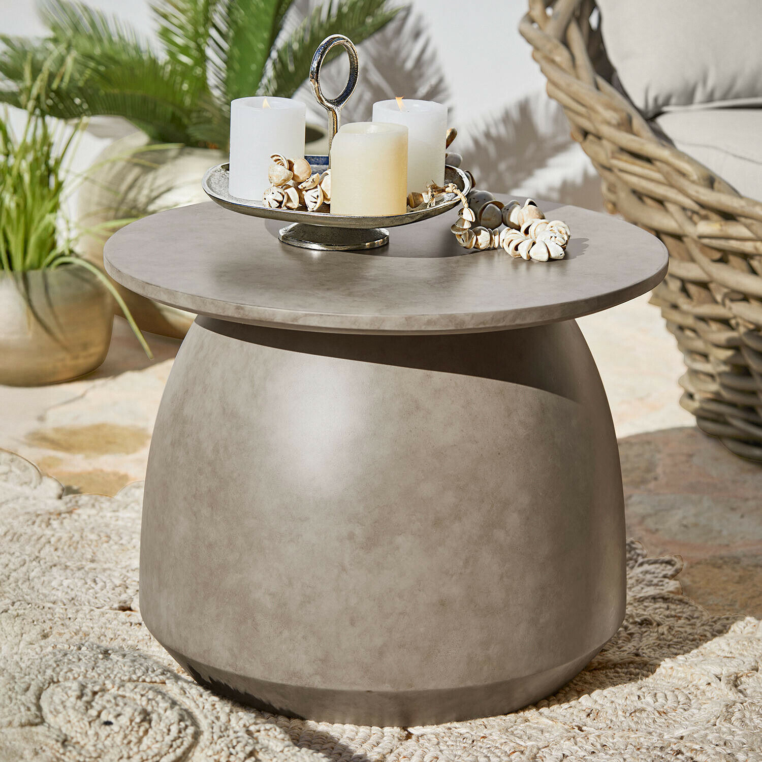 Ronde salontafel van grijs beton met kaarsen en schelpendecoratie op terras