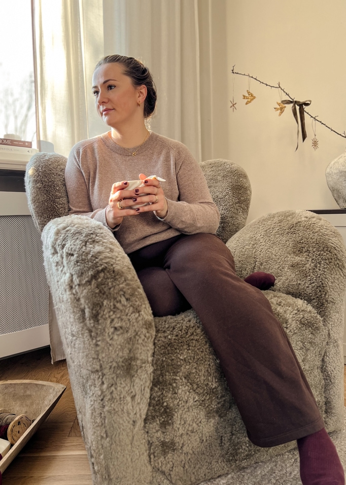 Zachte grijze kunstbont fauteuil in gezellige kamer met vrouw die een kop vasthoudt